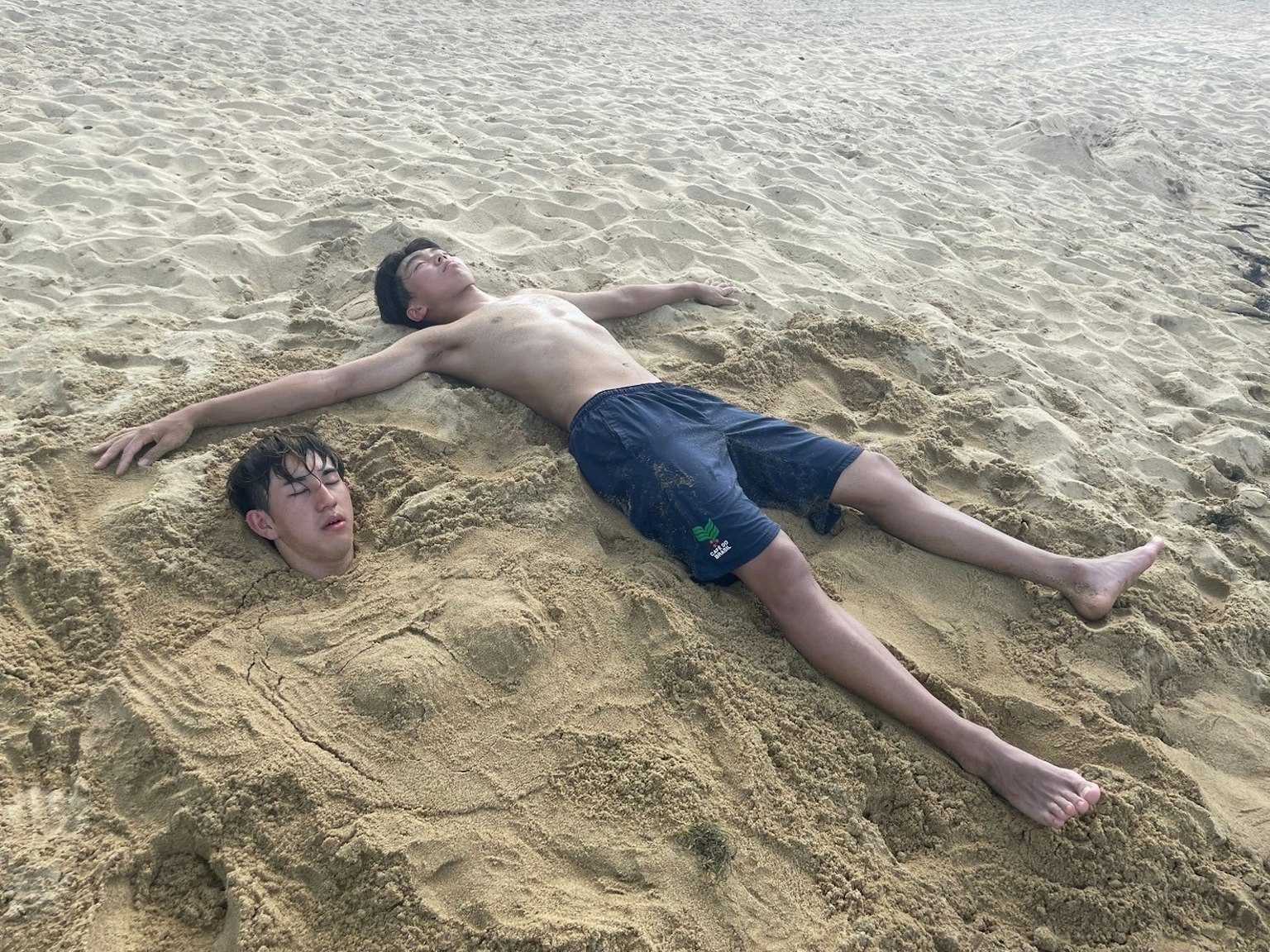 两个男孩在沙滩上顽皮地埋在沙子里