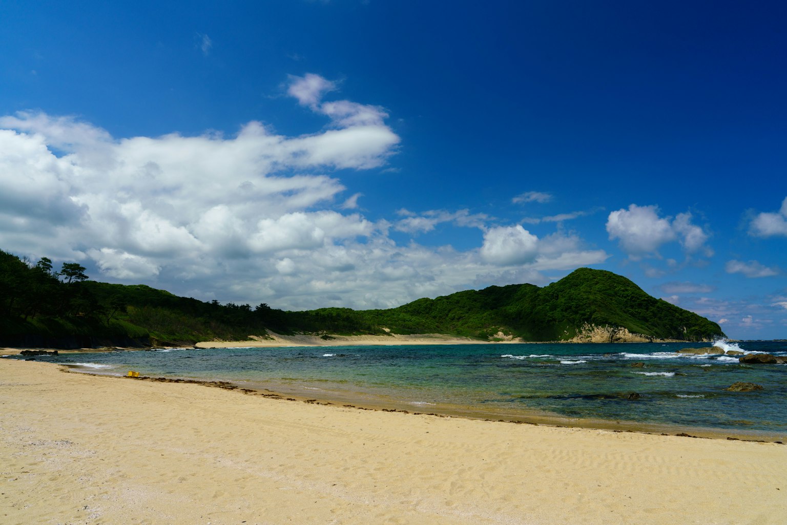 ทิวทัศน์ชายหาดที่สวยงามพร้อมท้องฟ้าสีฟ้าและเมฆสีขาวเนินเขาสีเขียวและทะเลสงบ