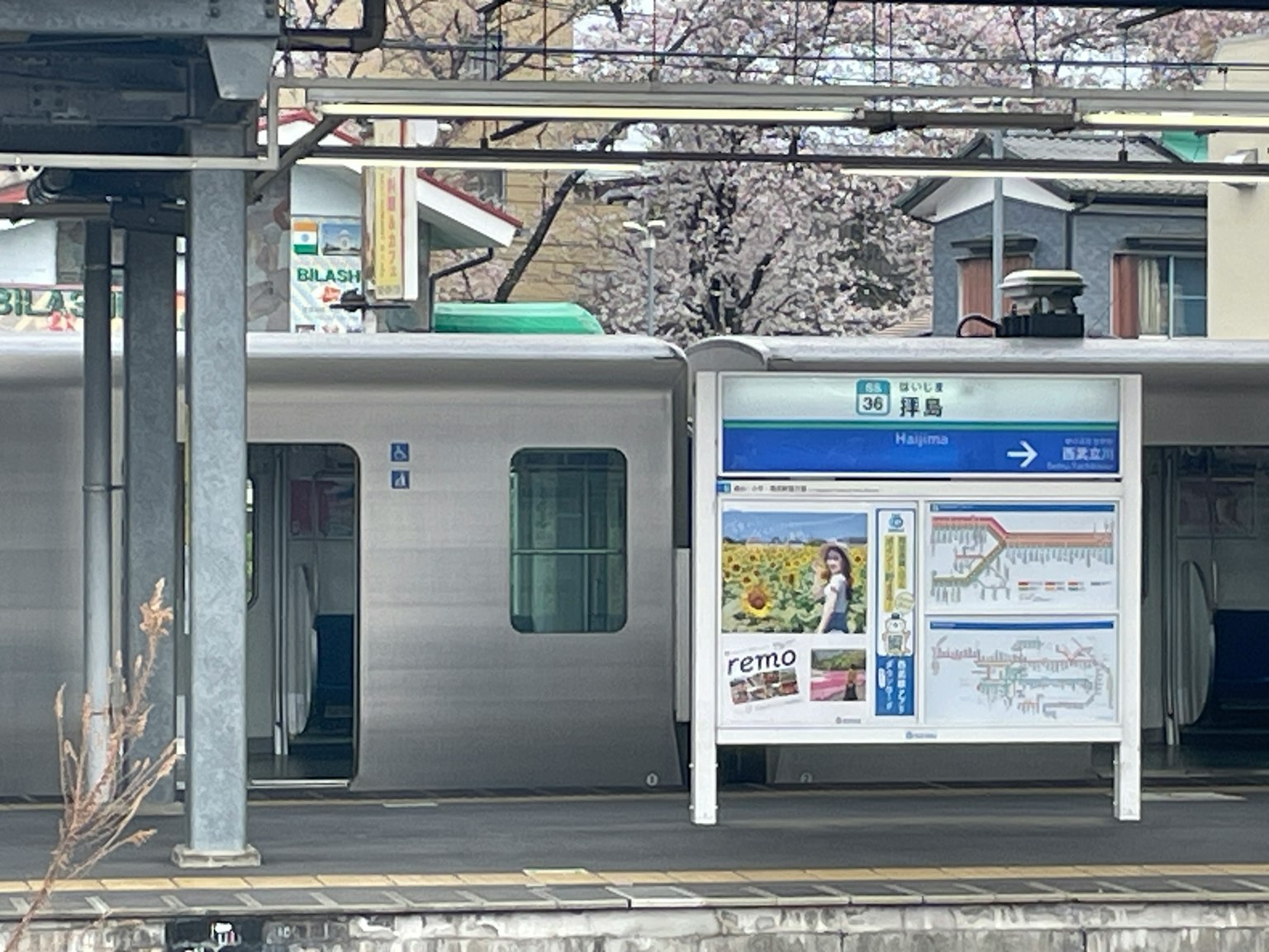 รถไฟจอดที่ชานชาลาพร้อมป้ายข้อมูล ต้นซากุระอยู่ในพื้นหลัง