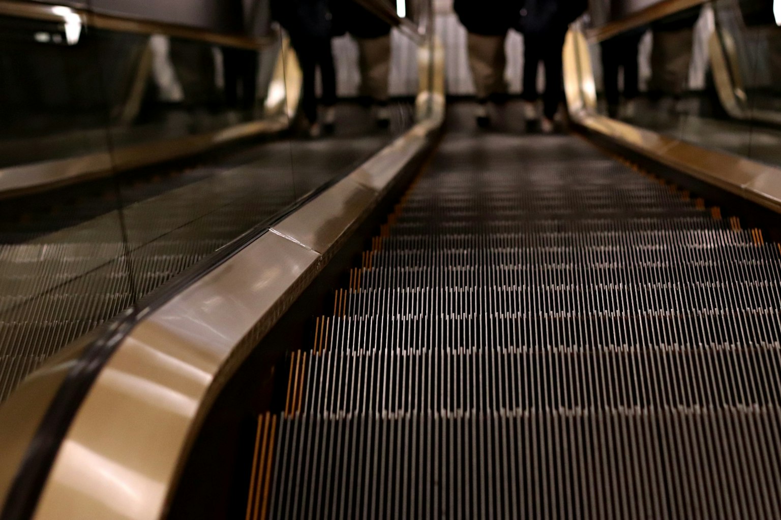 Vue du bas d'un escalator montrant des rampes dorées et des marches métalliques