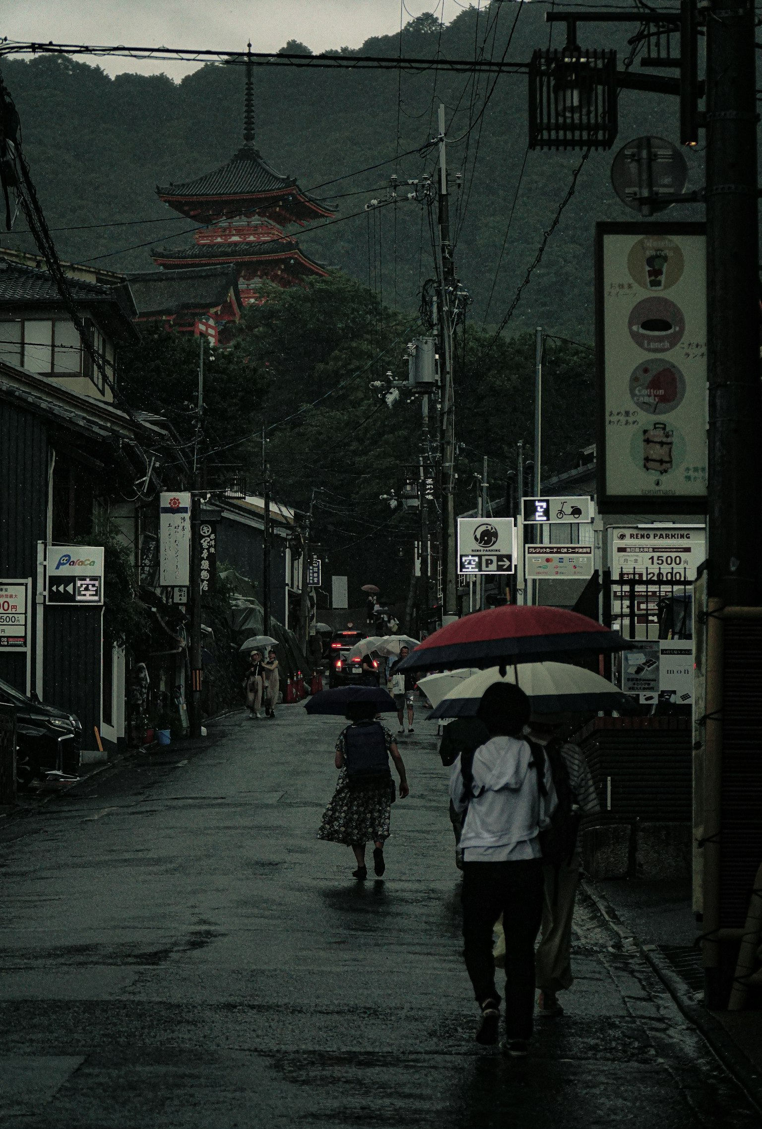 Calle tranquila con personas caminando bajo la lluvia y un templo al fondo