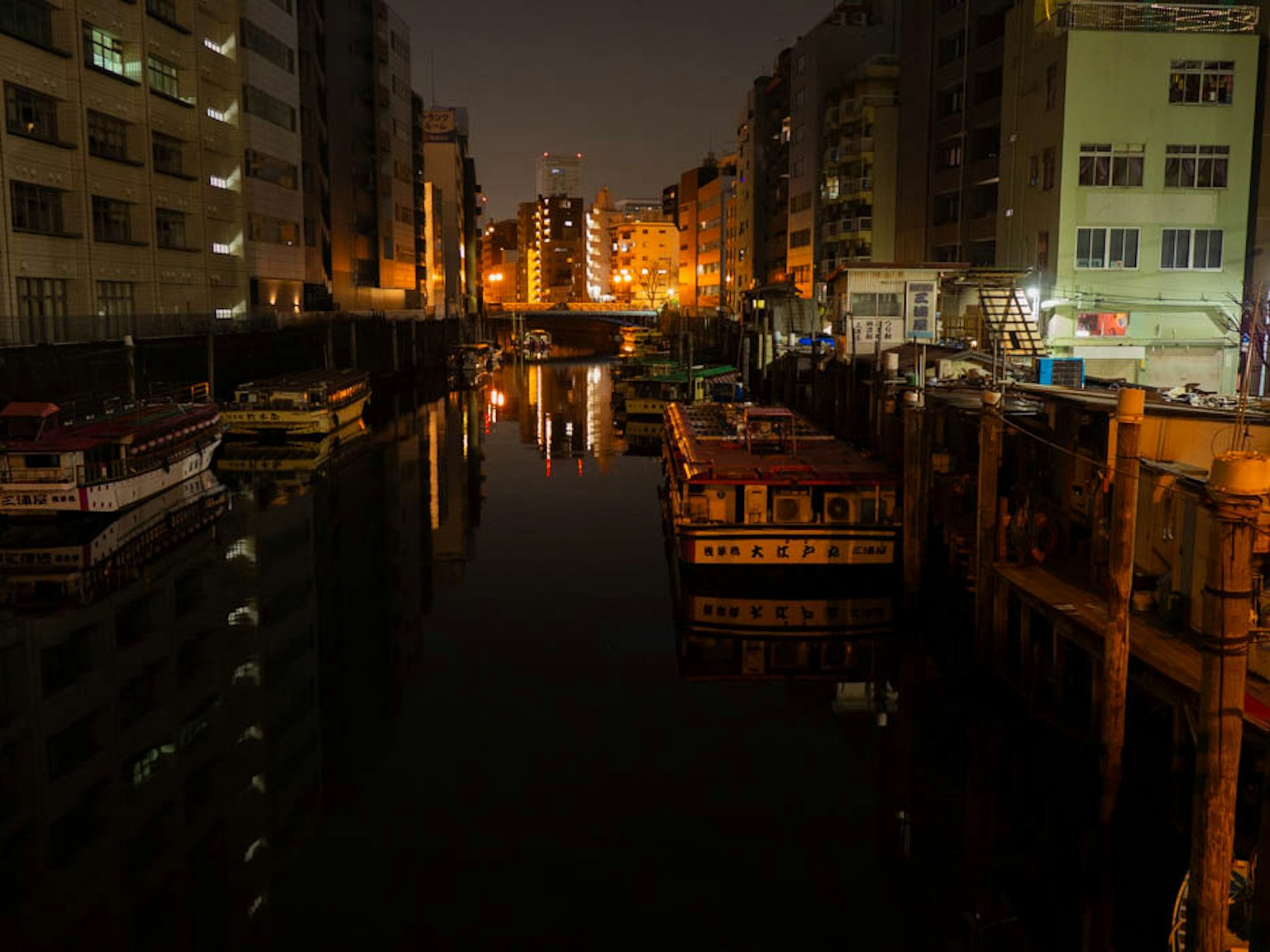 Vista nocturna de barcos en un canal con reflejos de edificios