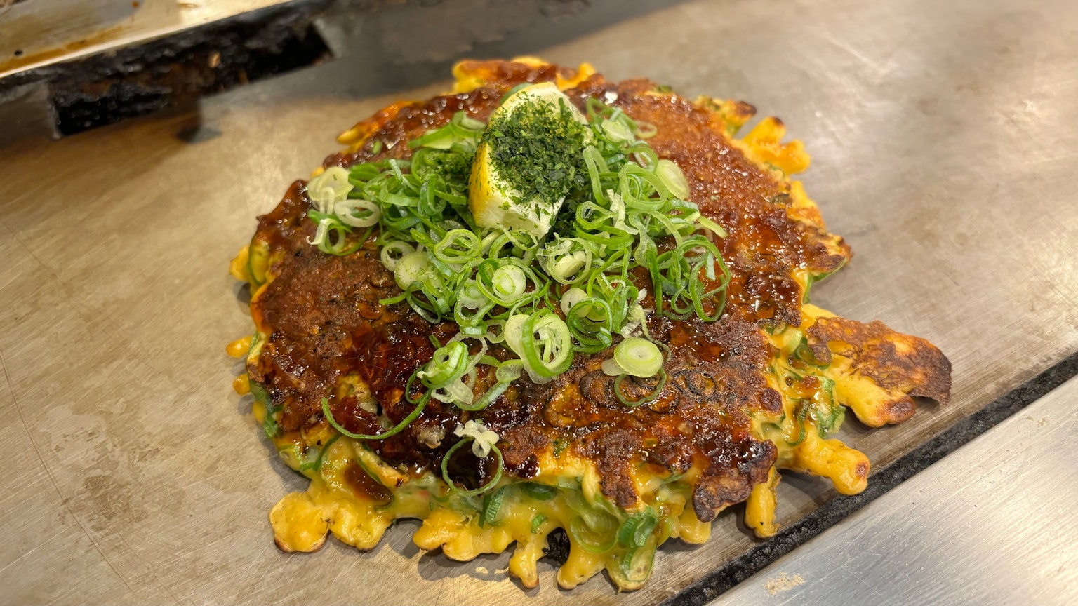 Okonomiyaki cubierto con cebollín y limón en una parrilla caliente