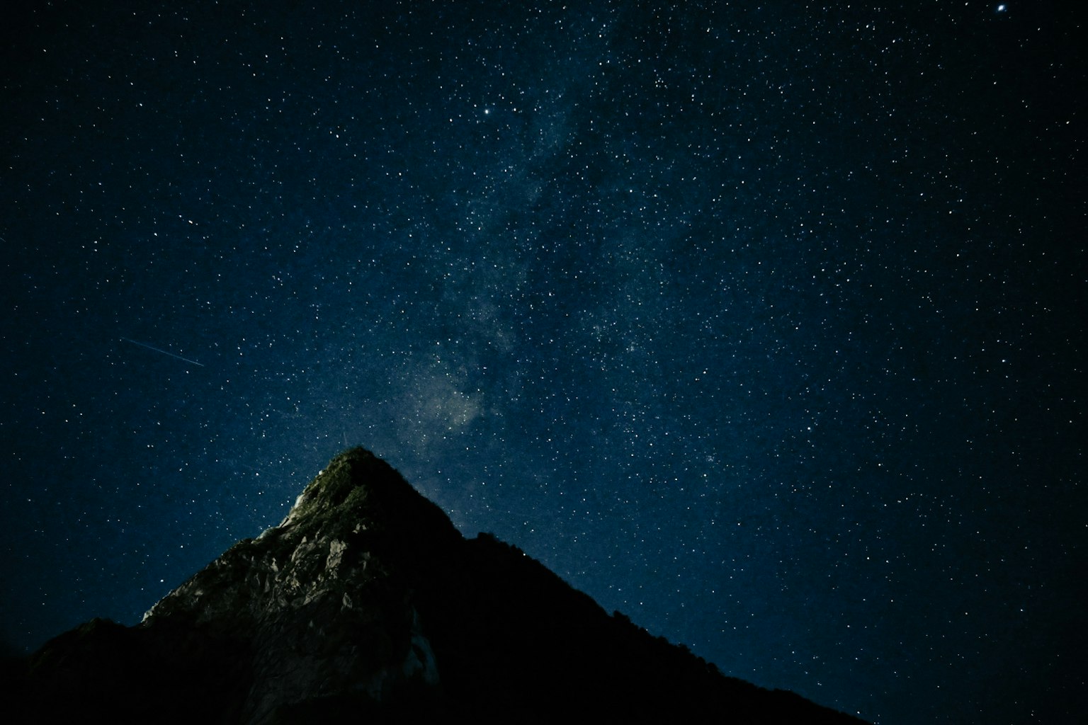 星空の下にそびえる山の頂上が見える夜景
