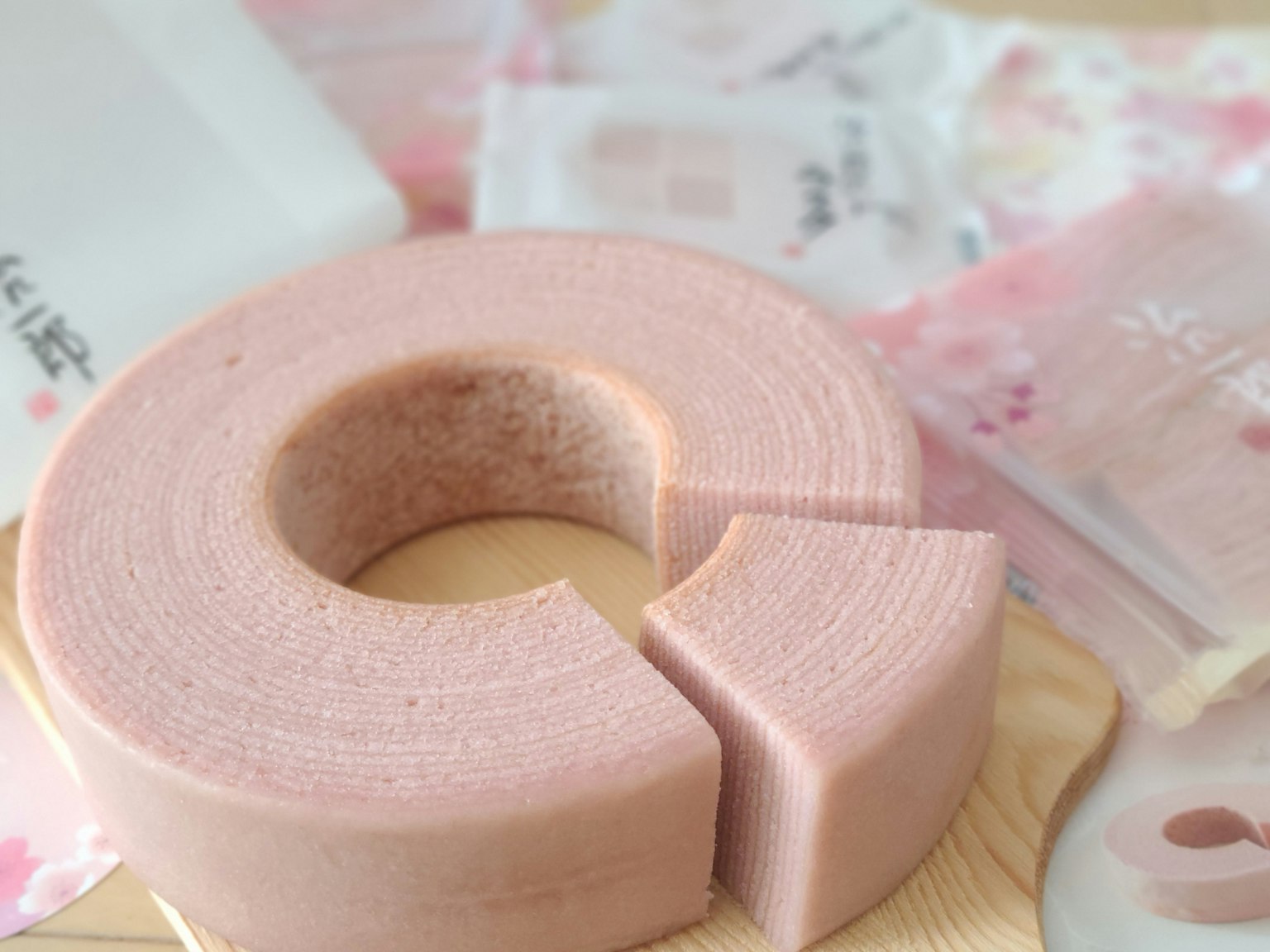 Un Baumkuchen rosa con una fetta tagliata posato su un piatto di legno circondato da imballaggi
