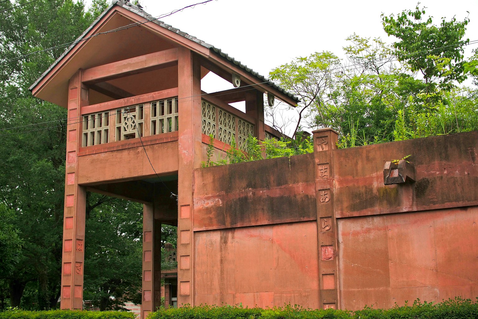 A raised structure with brown walls surrounded by green trees