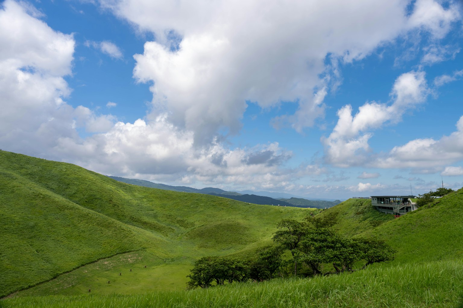 Bukit hijau di bawah langit biru dengan awan putih dan sebuah rumah