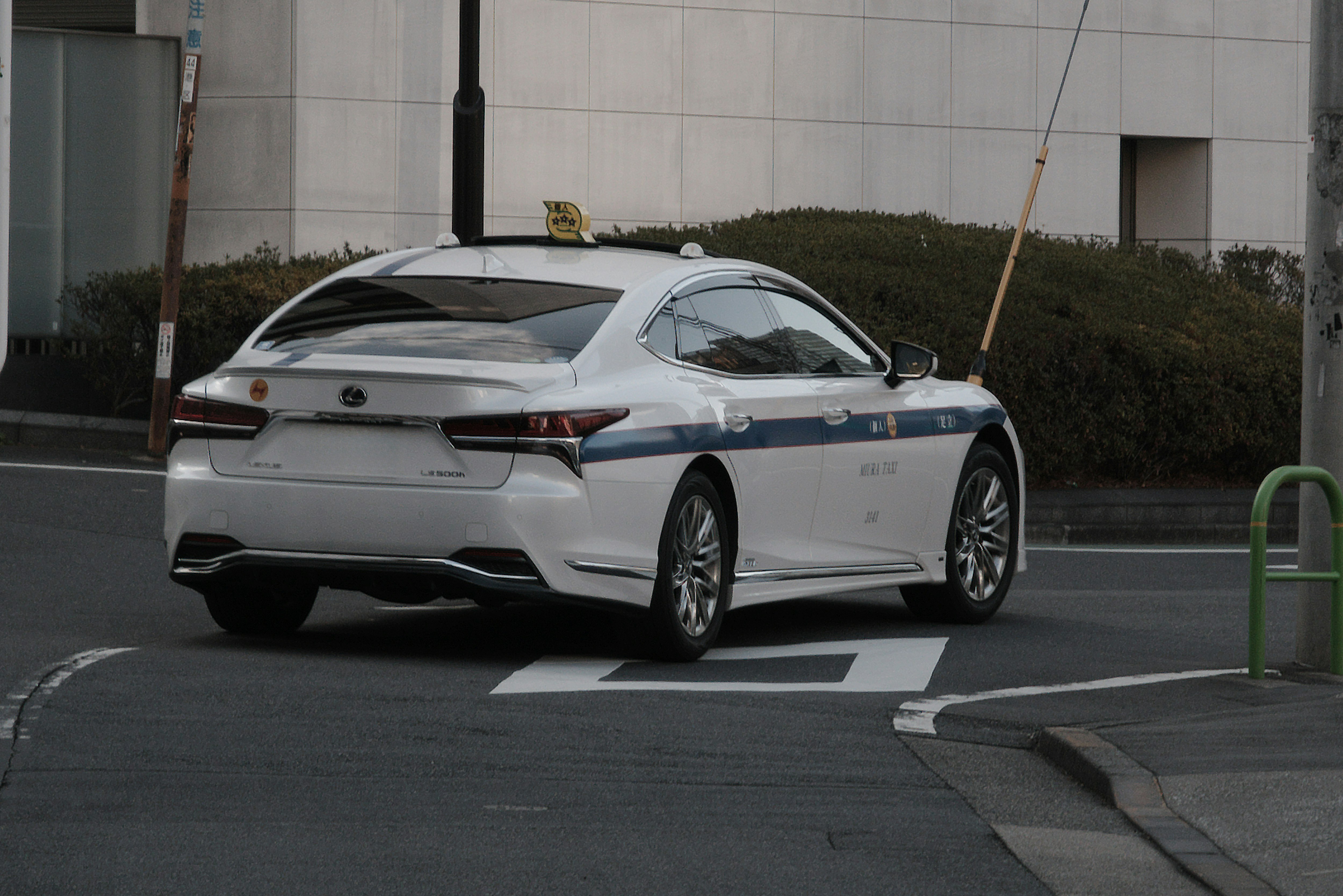White Lexus sports sedan driving on a road in front of a building