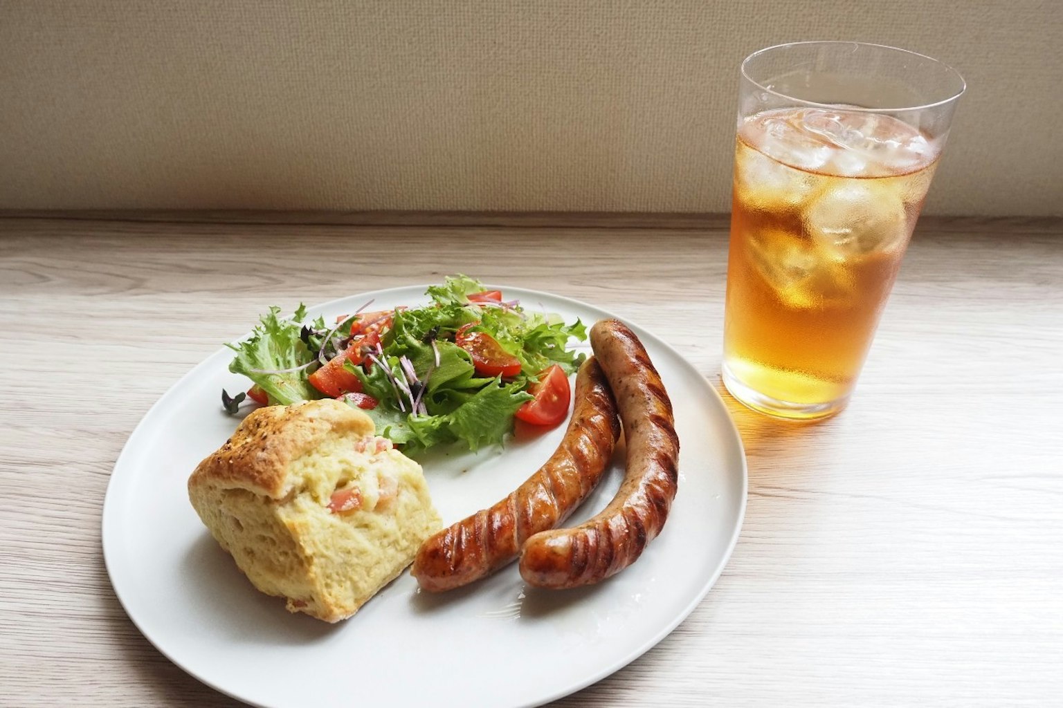 Une assiette avec de la salade, des saucisses, un biscuit et du thé glacé