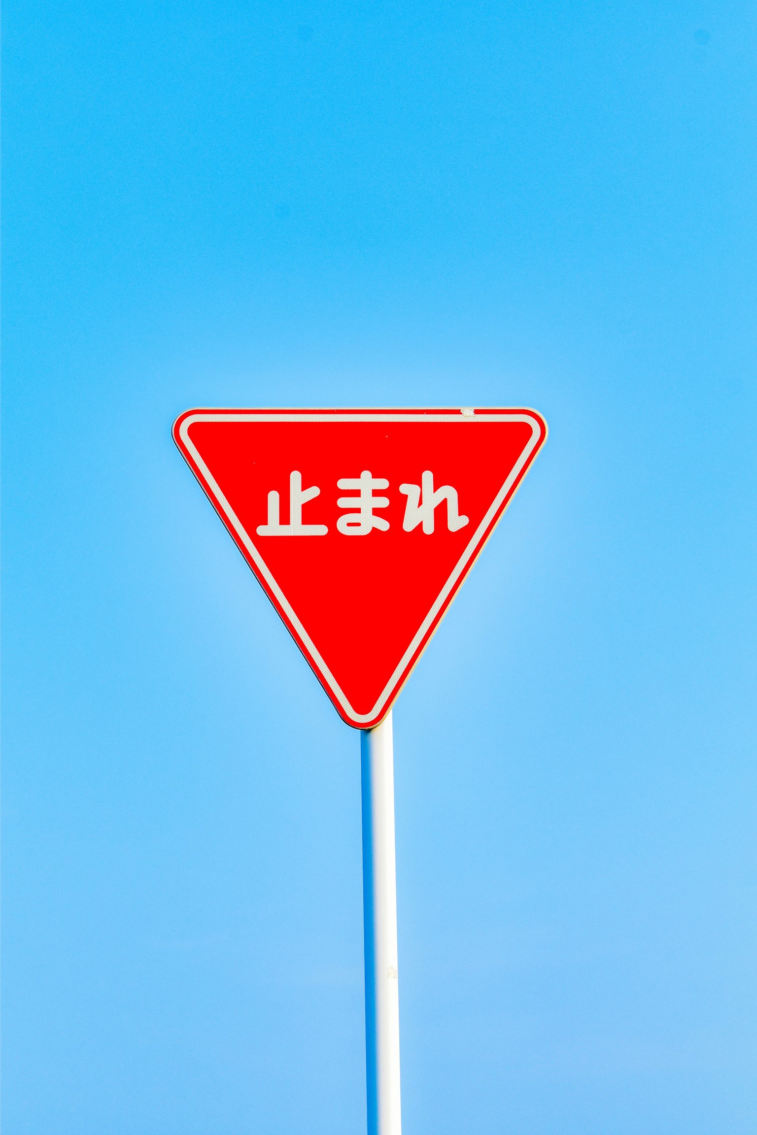 青空の下にある赤い三角形の止まれの標識
