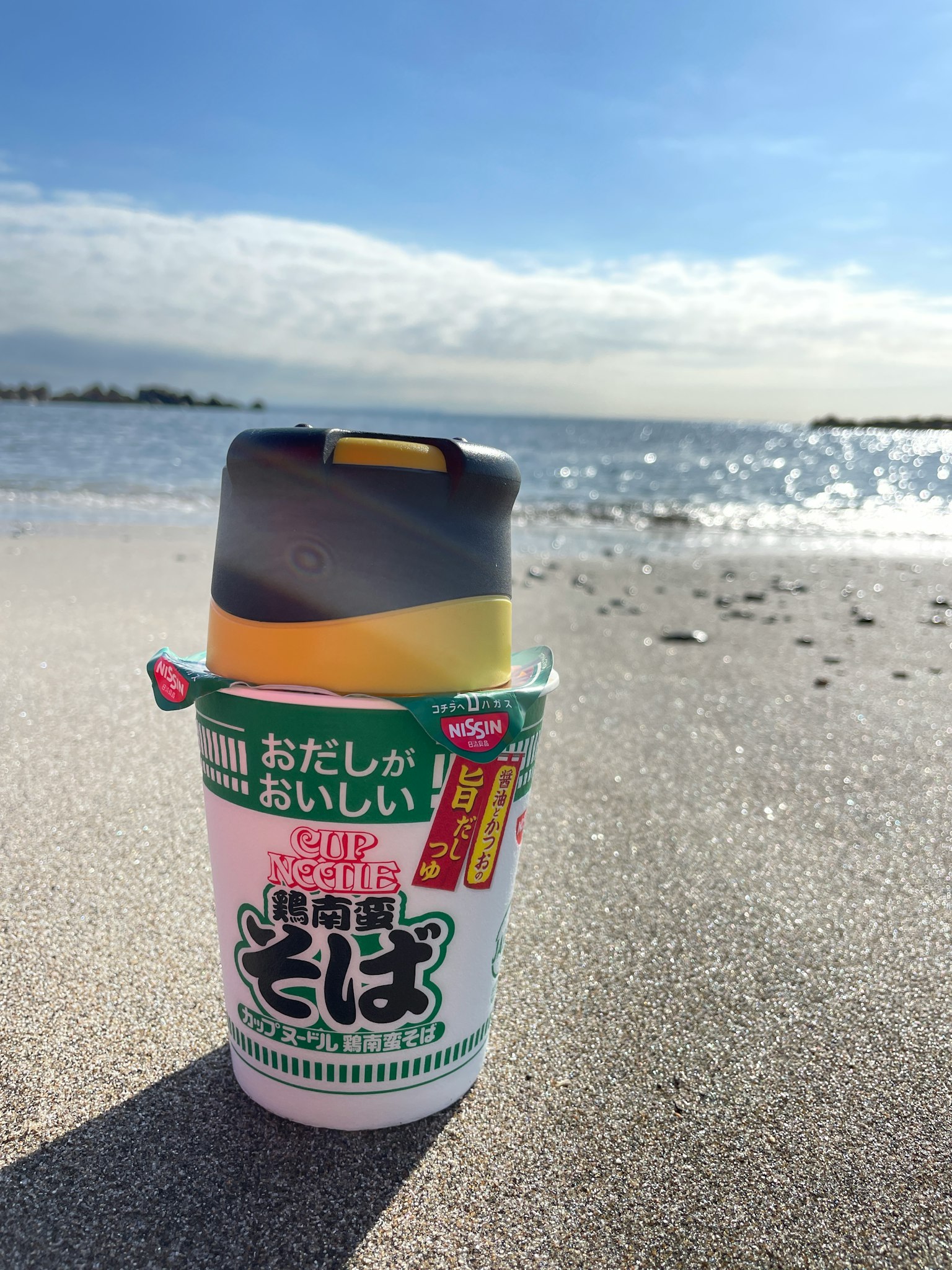 Taza de fideos soba colocada sobre la arena de la playa