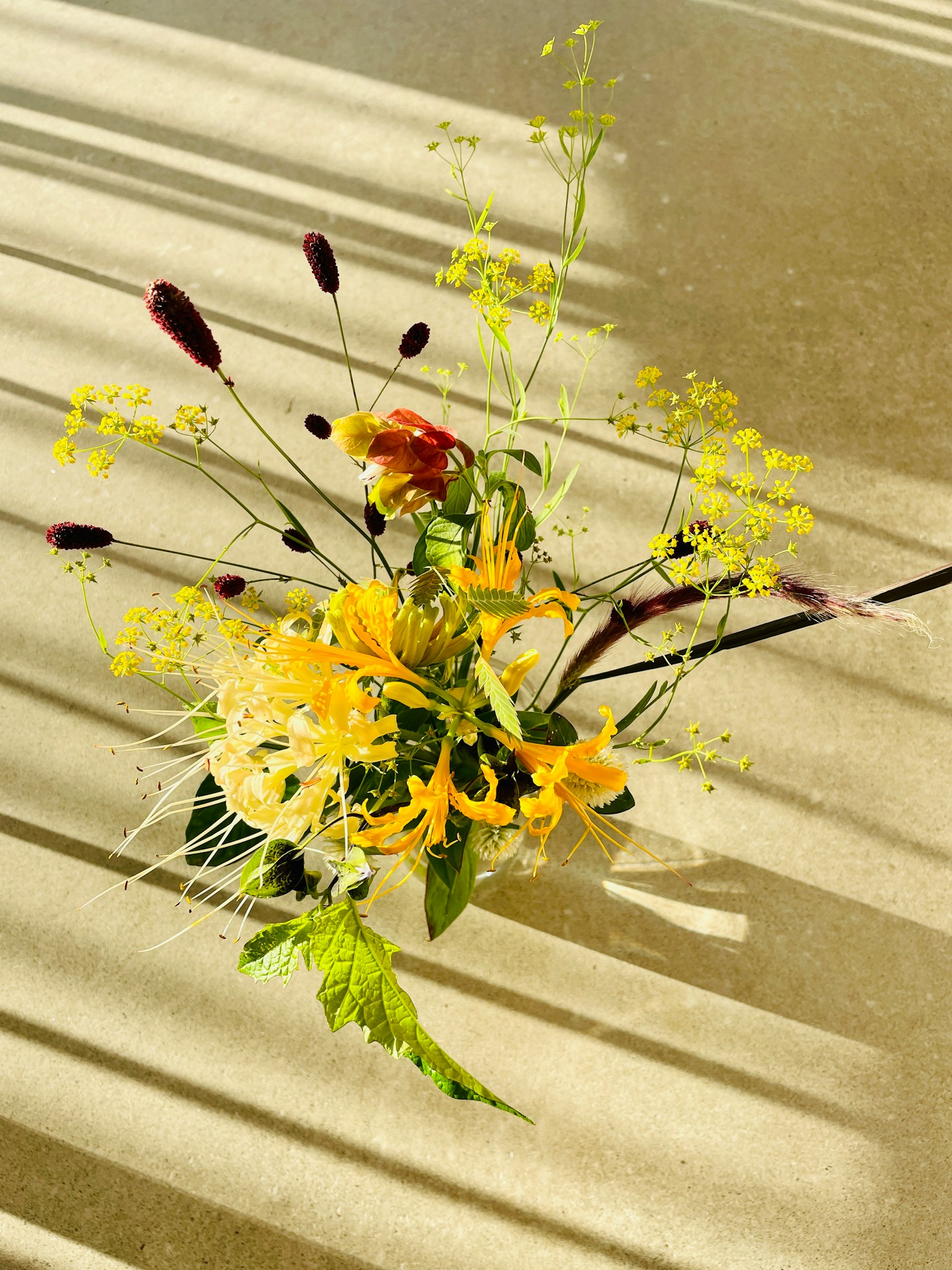 Hermoso arreglo de flores amarillas y hojas verdes colocado sobre una superficie con sombras