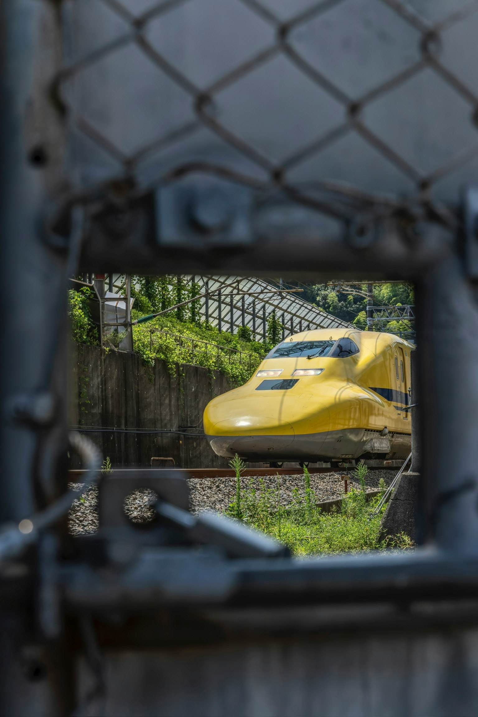 Yellow Shinkansen train visible through a fence