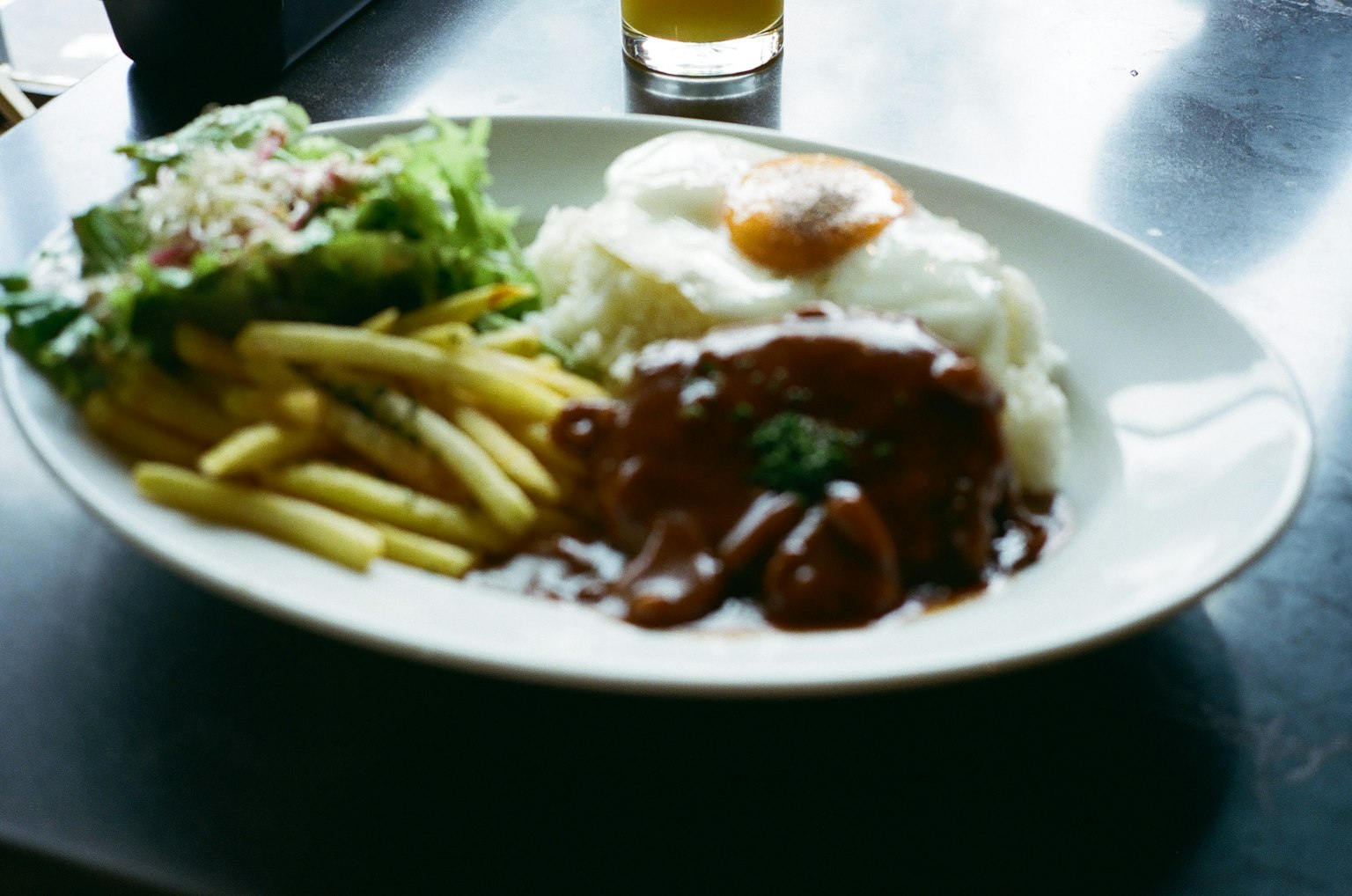 A plate with rice, fried egg, meat with gravy, French fries, and salad