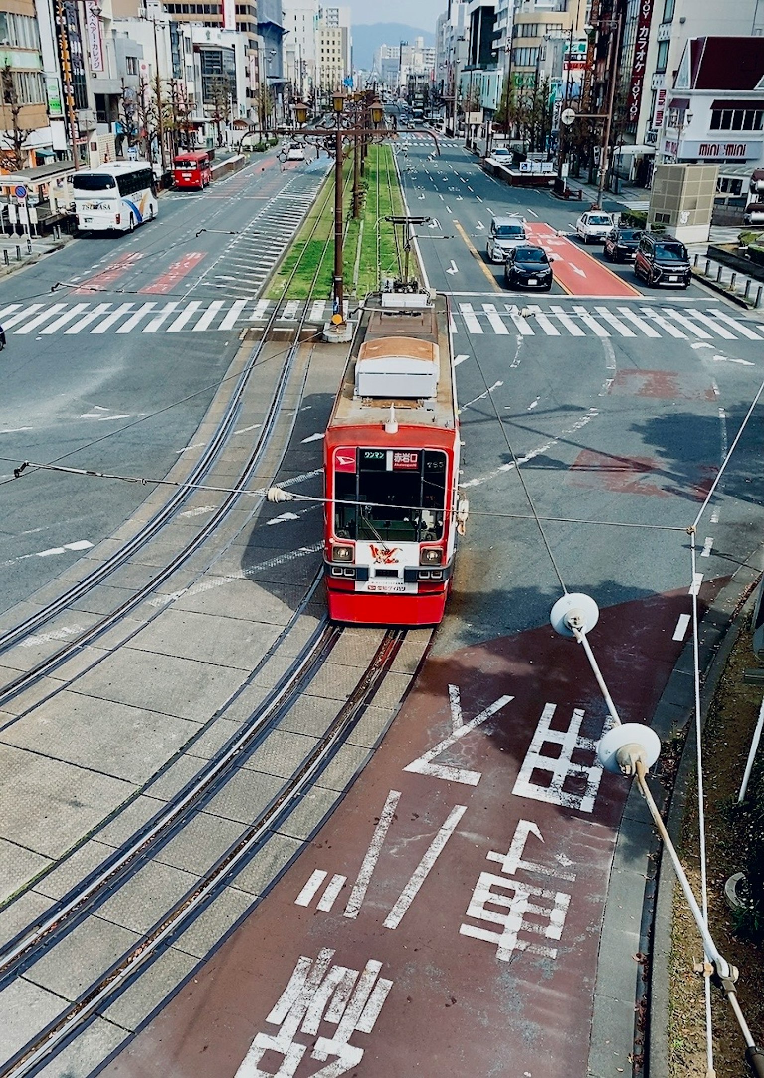 Rote Straßenbahn, die eine Kreuzung mit Gebäuden entlang der Straße überquert