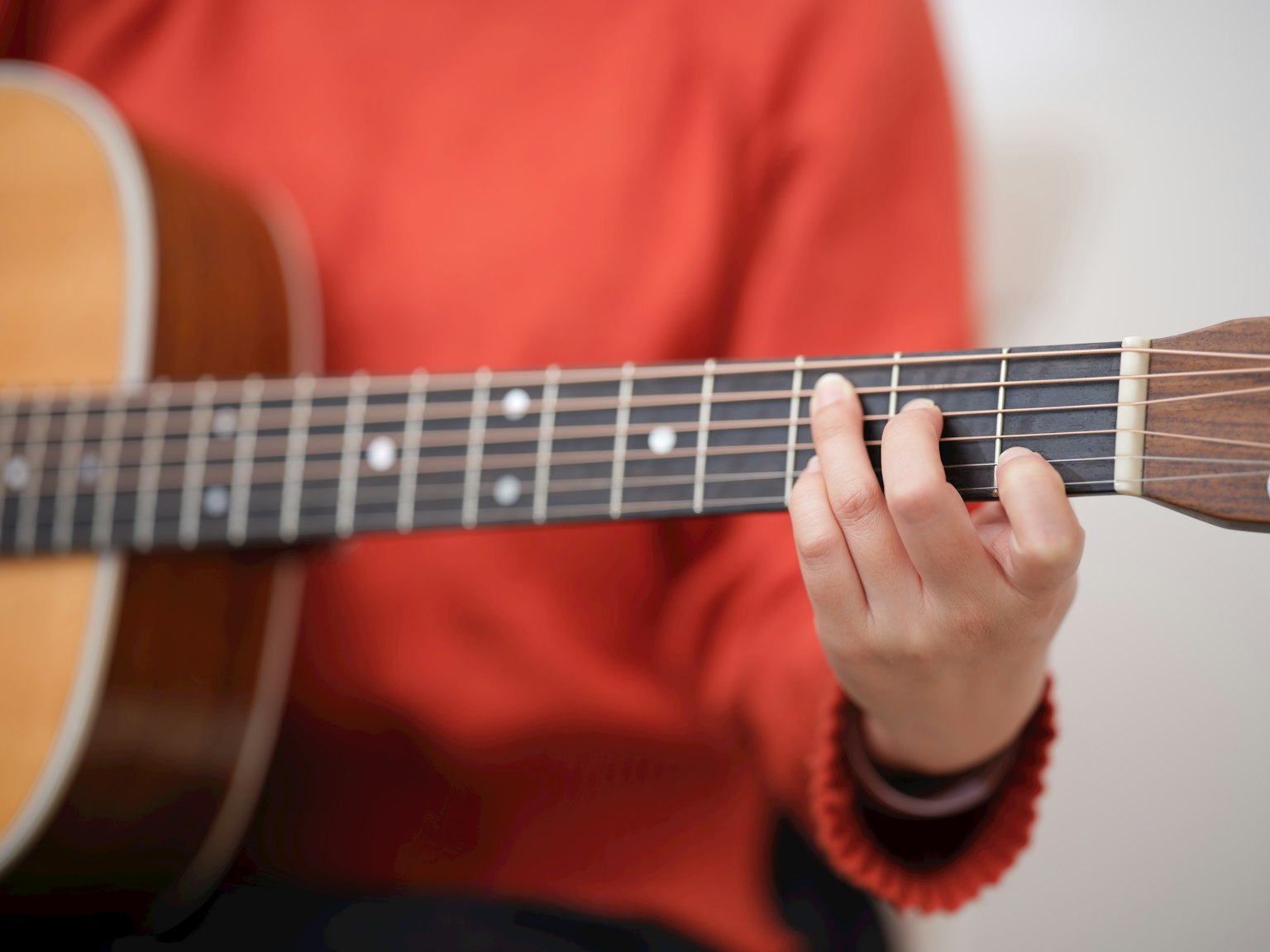 Kedekatan seseorang yang mengenakan sweater oranye memainkan gitar akustik
