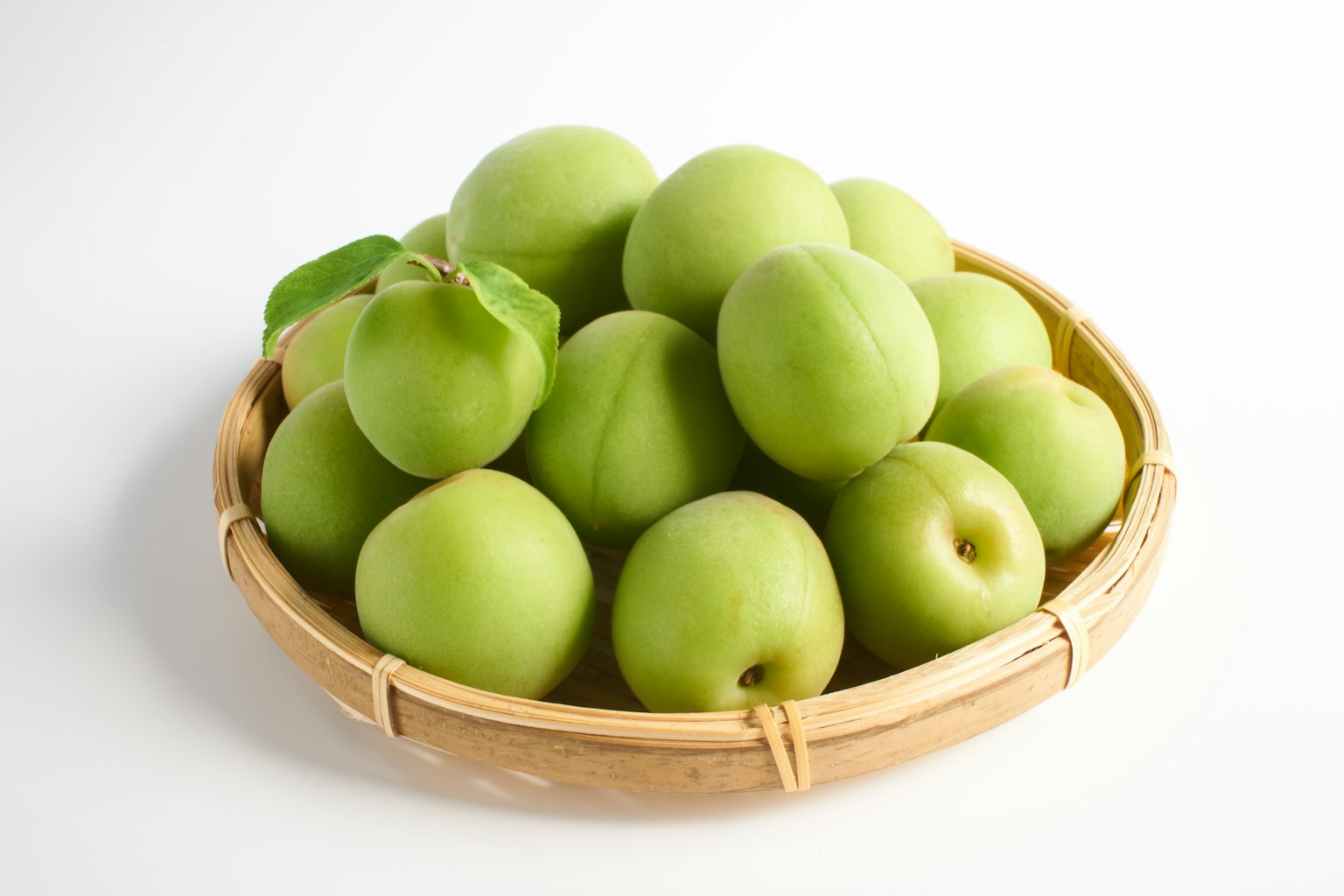 Green plums arranged in a bamboo basket