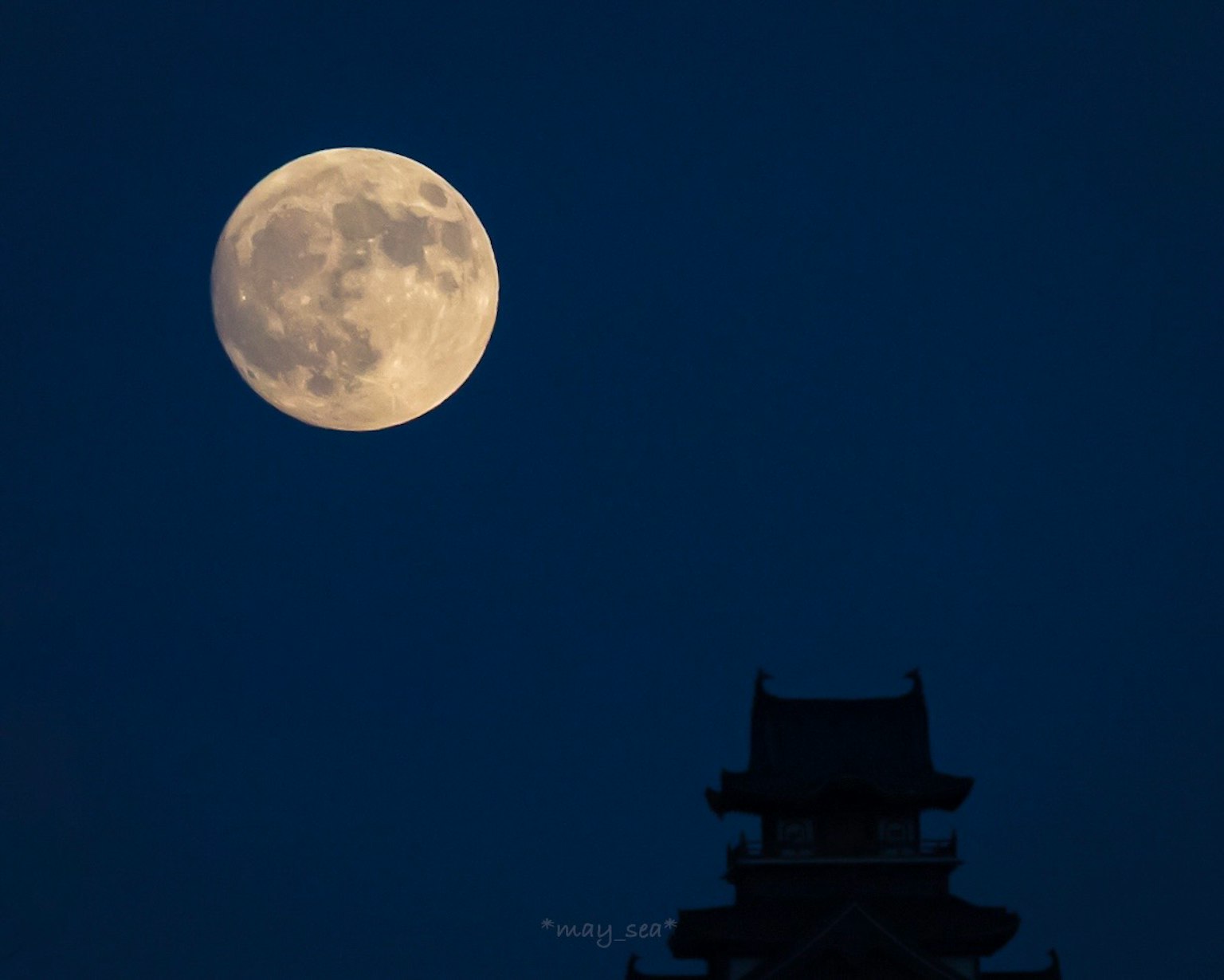 Large full moon in the night sky with a silhouetted tower