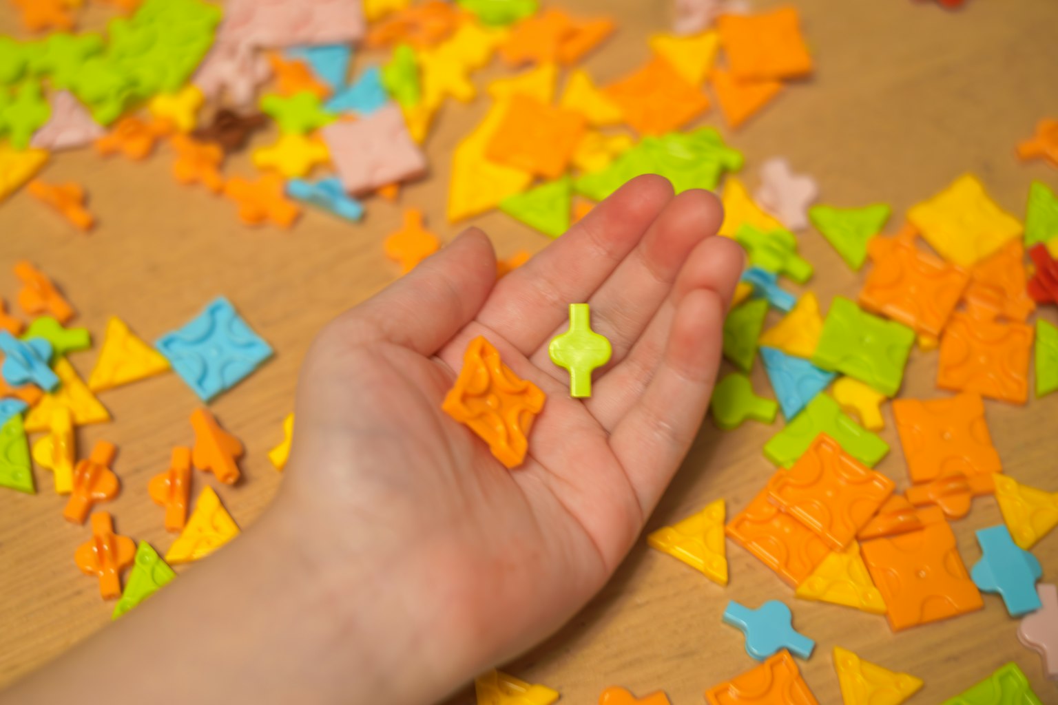 Eine Hand hält bunte Puzzlestücke mit vielen verstreuten Stücke auf einer Oberfläche