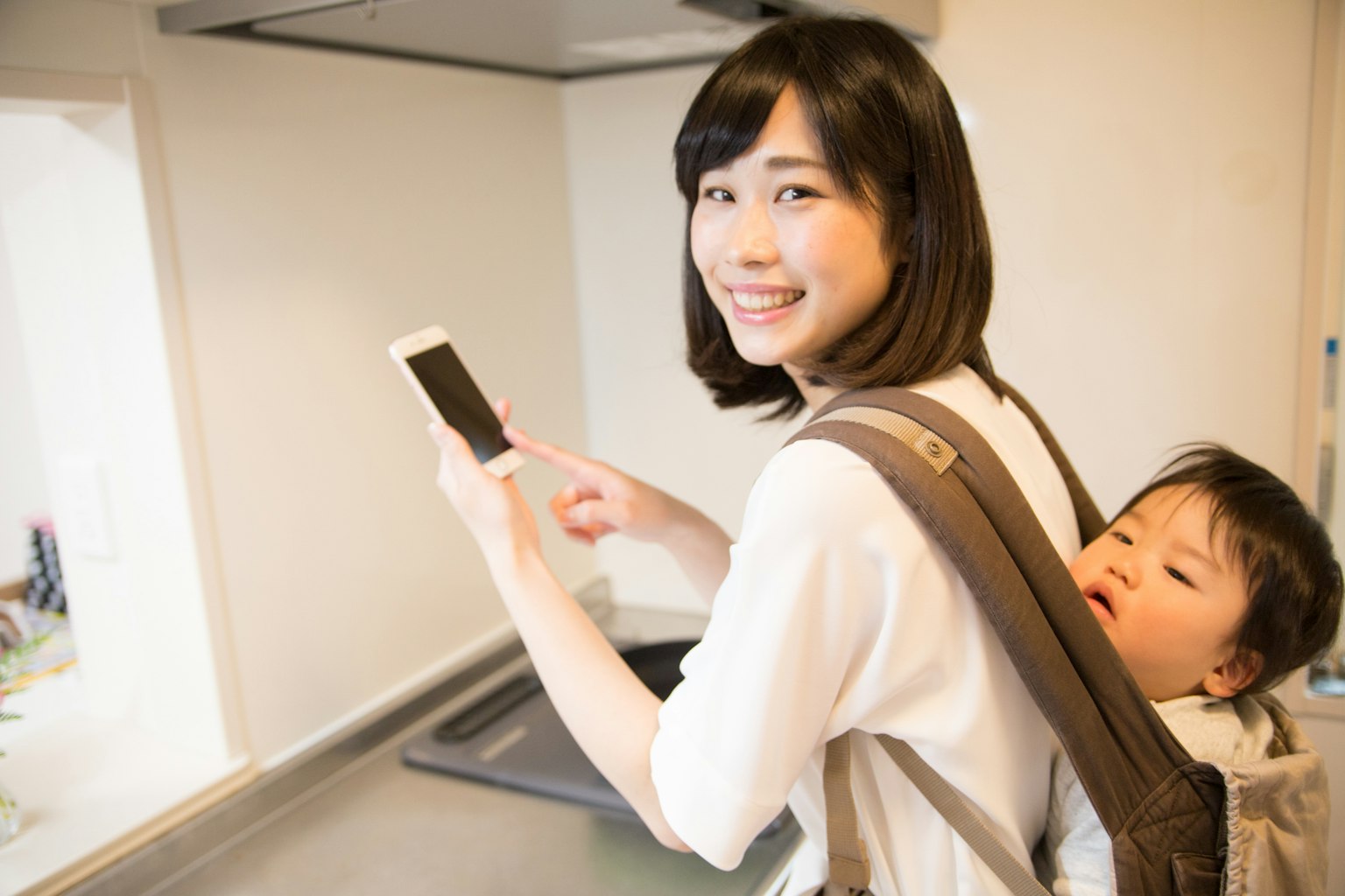 Mère utilisant un smartphone tout en portant un enfant sur le dos