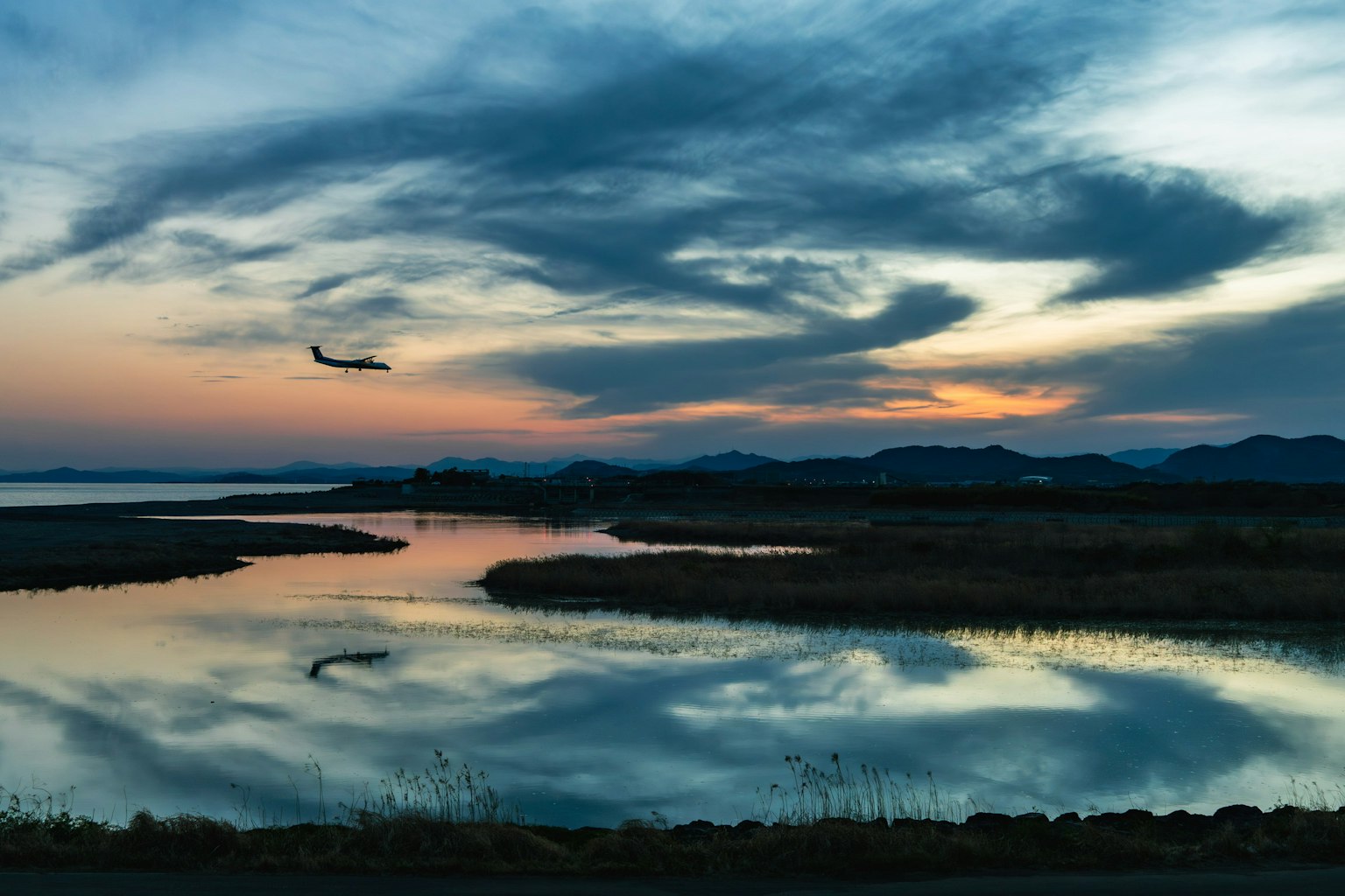Un paysage magnifique avec un avion volant contre un ciel de coucher de soleil réfléchissant des couleurs et des nuages sur la surface de l'eau