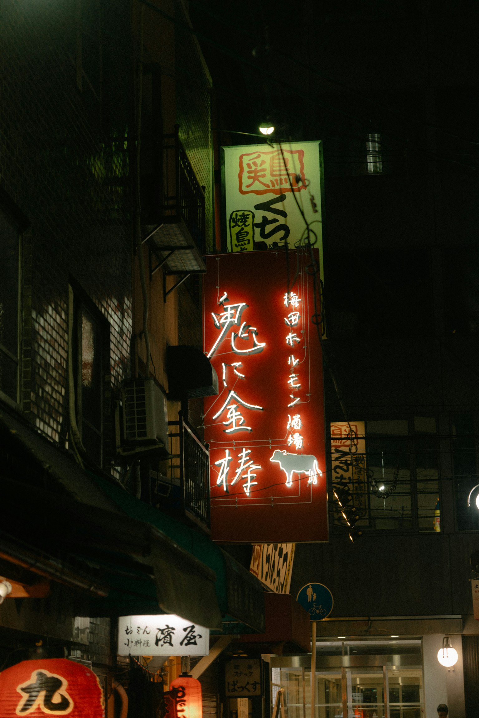 Rotiertes beleuchtetes Schild eines Izakaya mit dem Namen Oni ni Kanabo bei Nacht