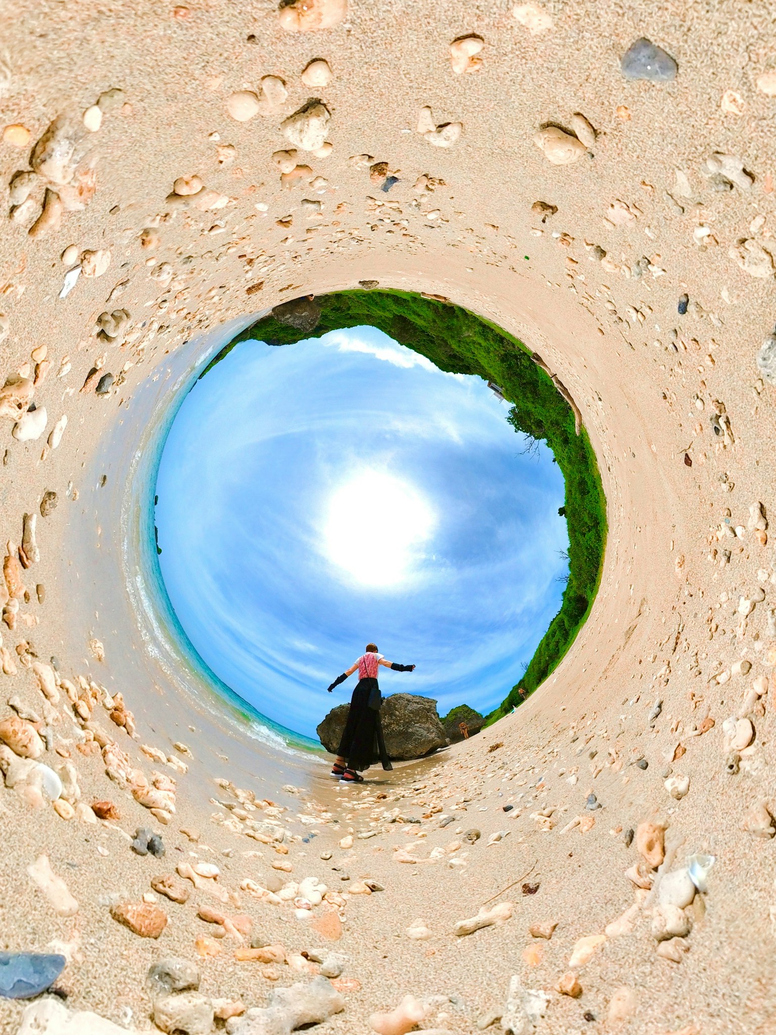 Eine Person steht im Zentrum eines Sandstrandes mit blauem Himmel und Sonne im Hintergrund