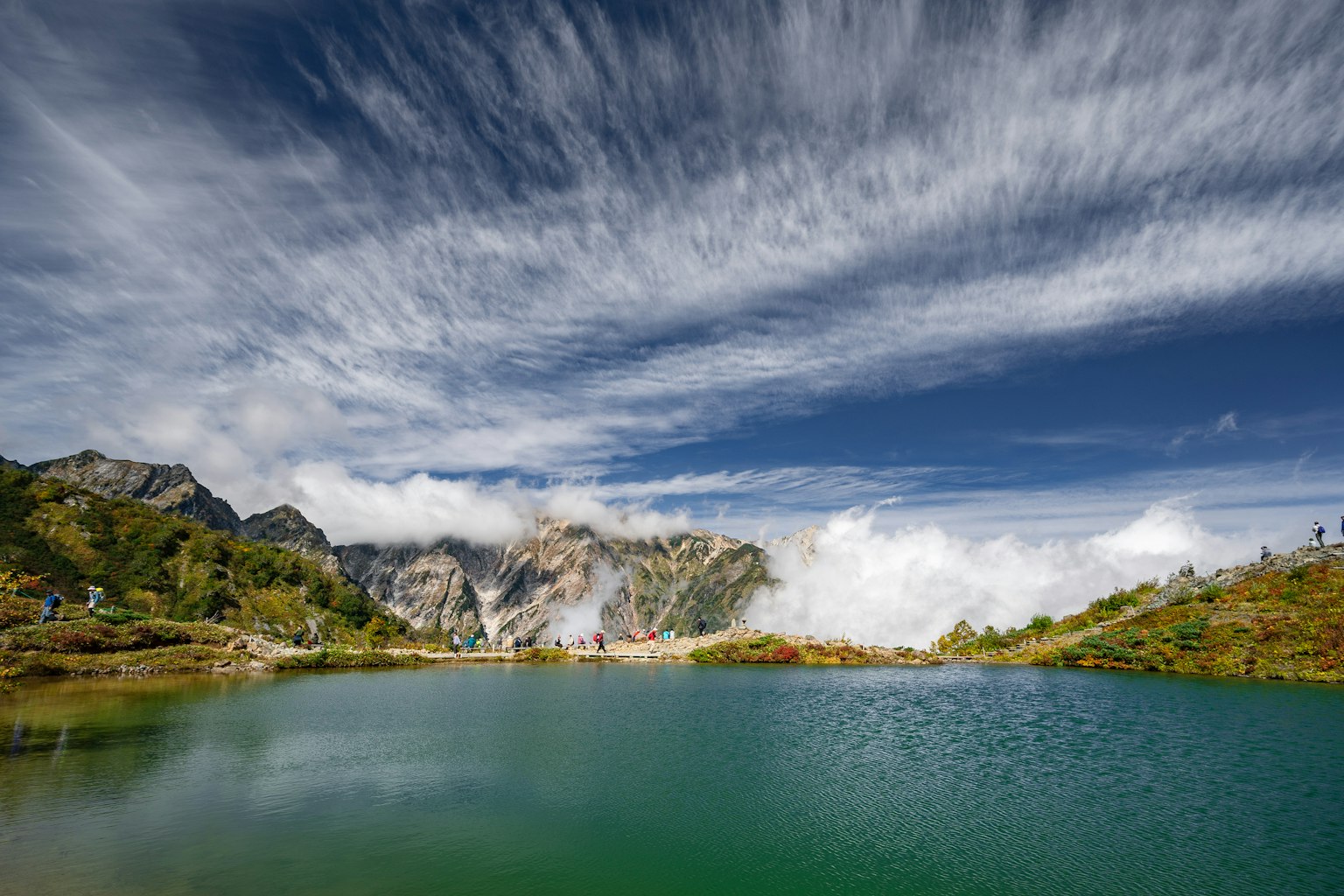Vista escénica de un lago rodeado de montañas con cielo azul y nubes delgadas
