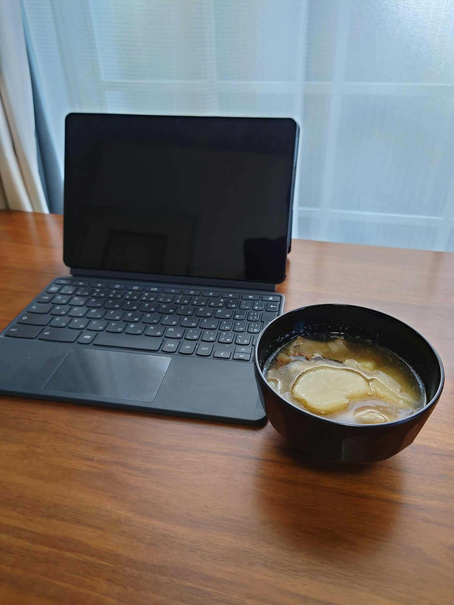 Table en bois avec une tablette et un bol noir de soupe avec des tranches de citron