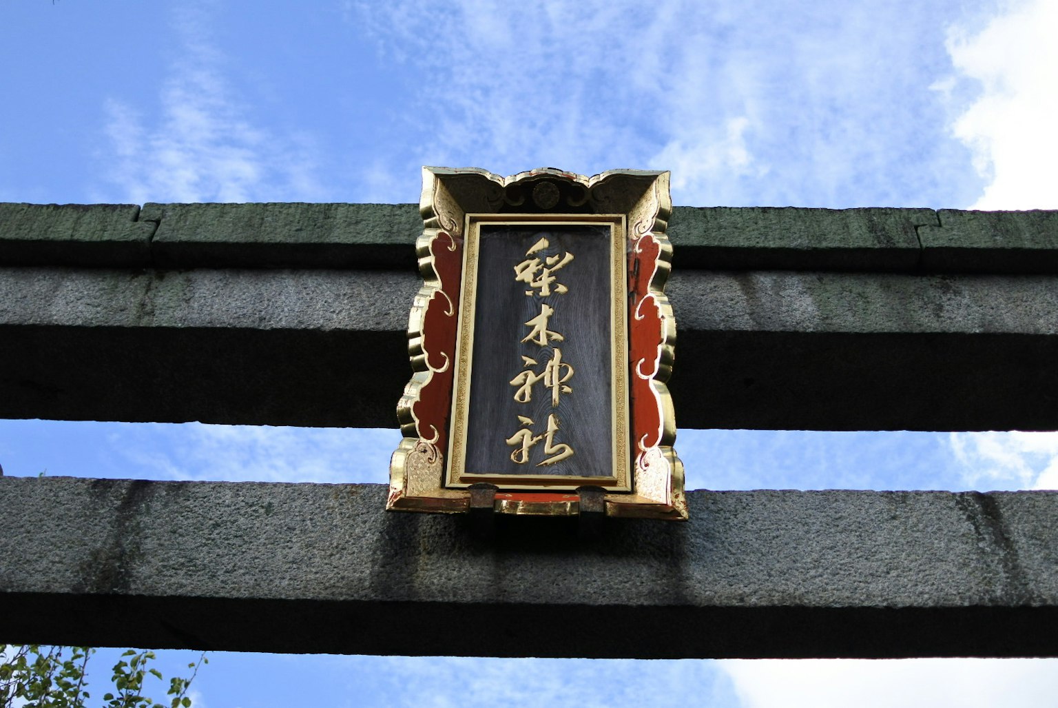 装饰性神社入口标志，红色和金色点缀，背景为蓝天