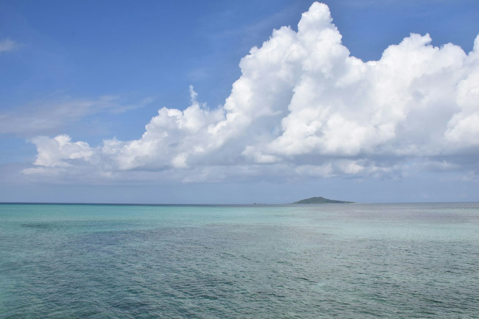 藍色海洋和白色雲朵的風景，遠處有一個小島