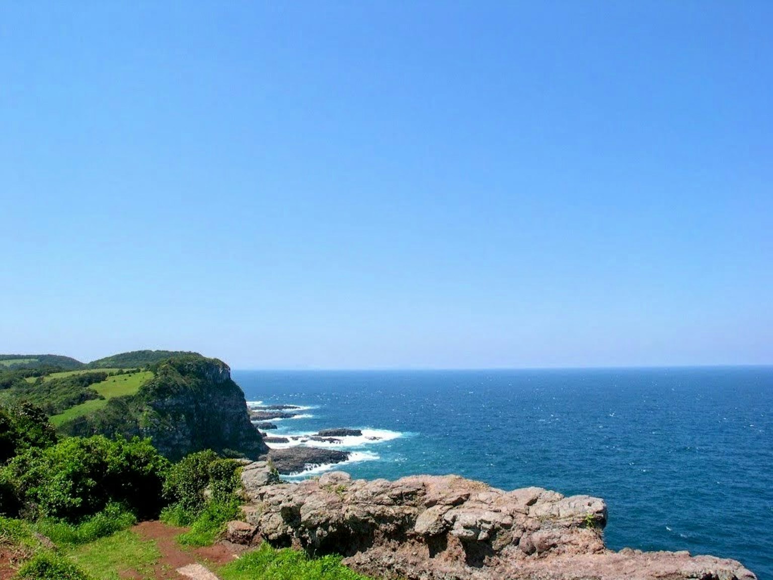 海岸風景藍色海洋和岩石海岸綠色丘陵和晴朗天空