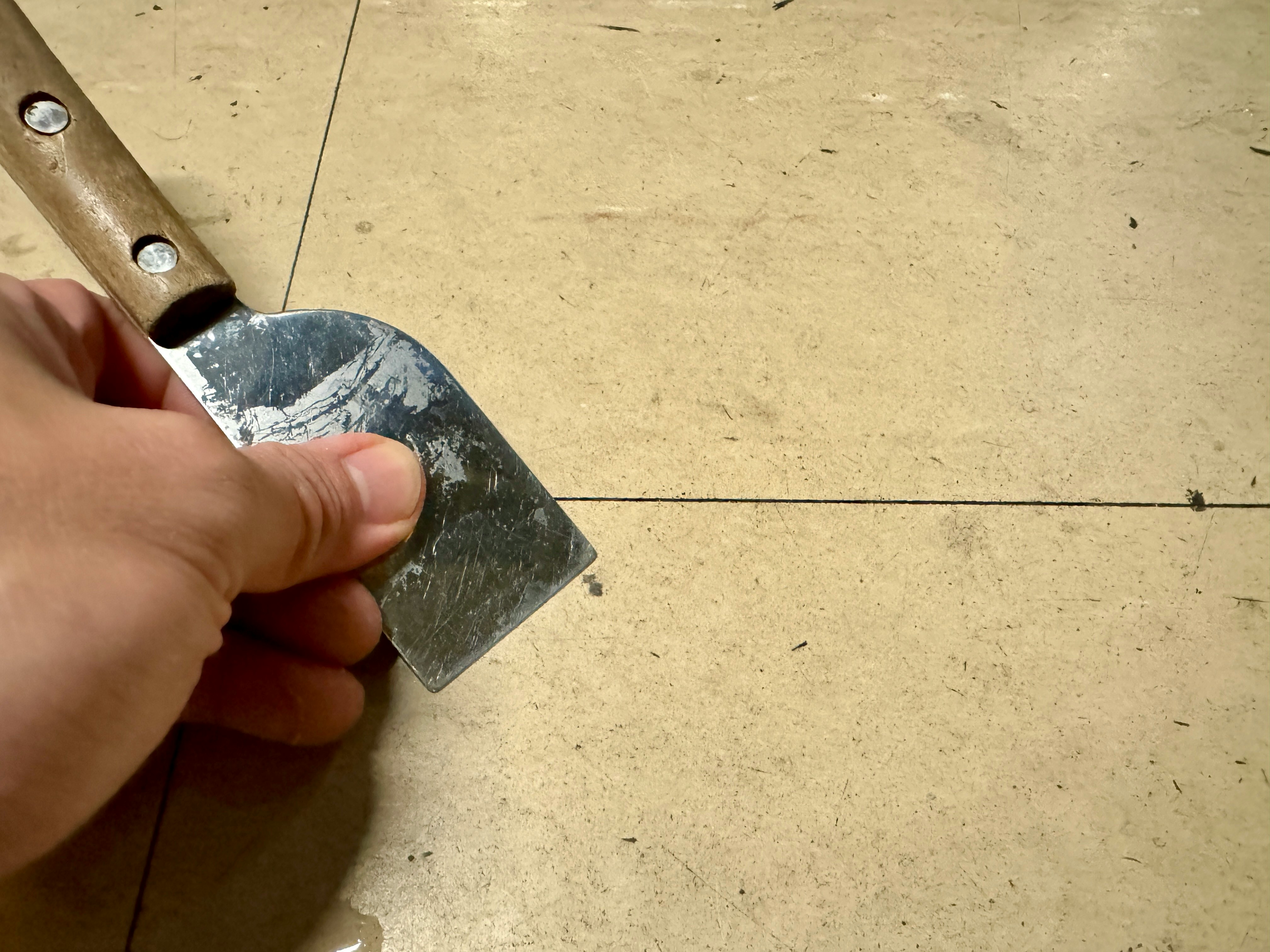 tangan memegang spatula sedang mengikis lantai beton