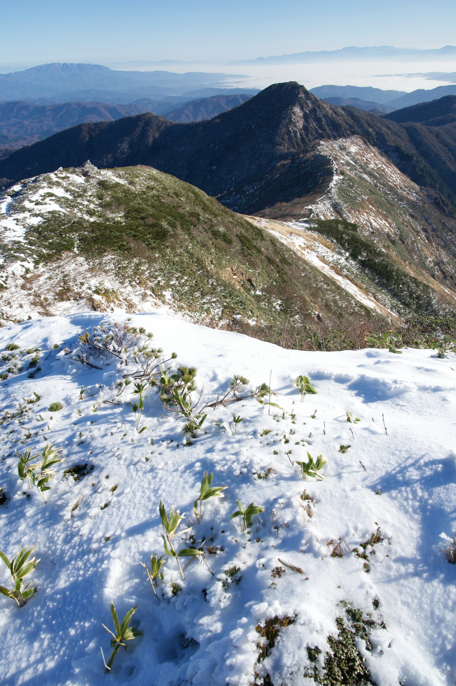 Paisaje montañoso cubierto de nieve con picos distantes y cielo azul claro