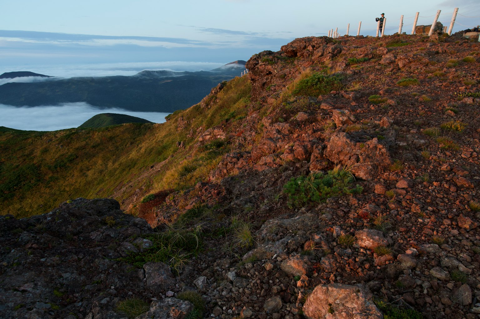 Rocky hillside with a view of the clouds below and a distant figure on the ridge