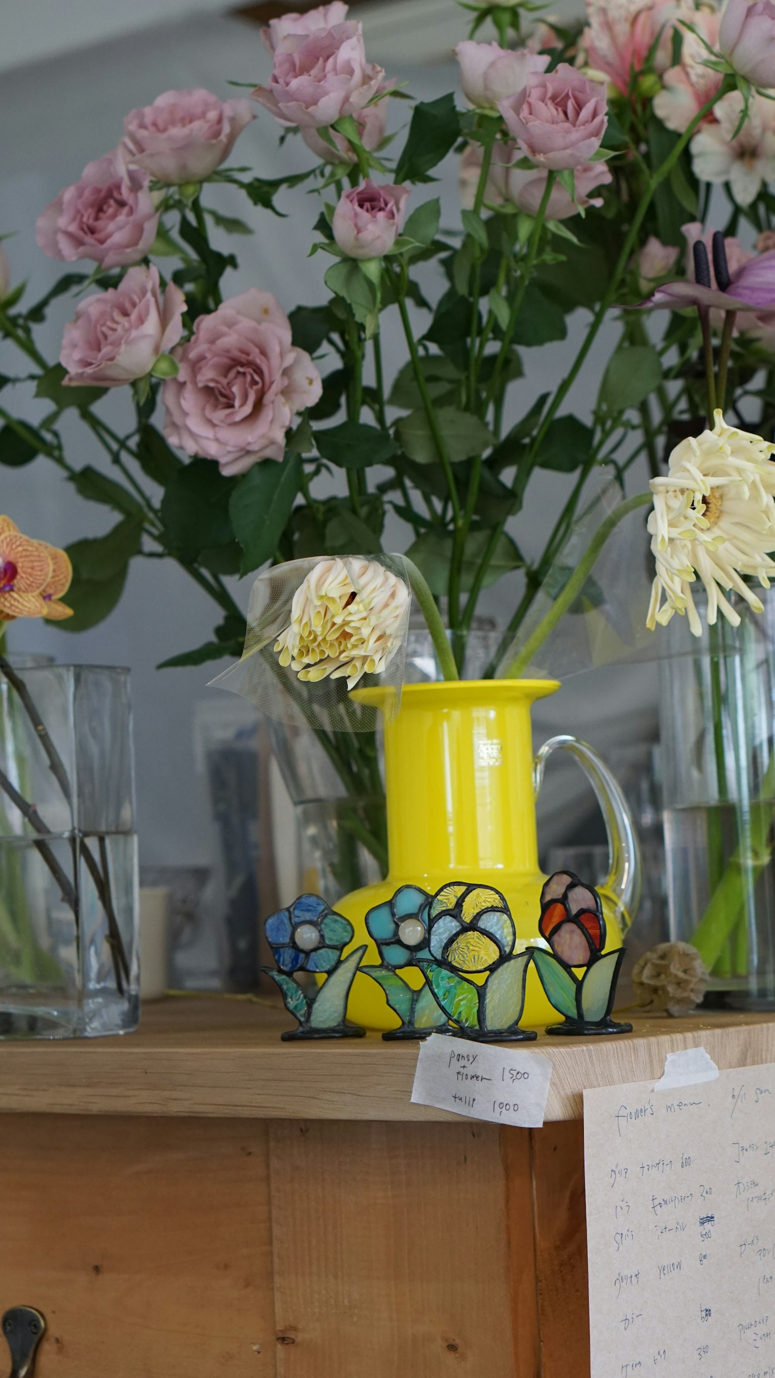 Ein lebhaft gelber Krug mit einem bunten Blumendesign steht auf einem Tisch, umgeben von rosa Rosen und anderen Blumen