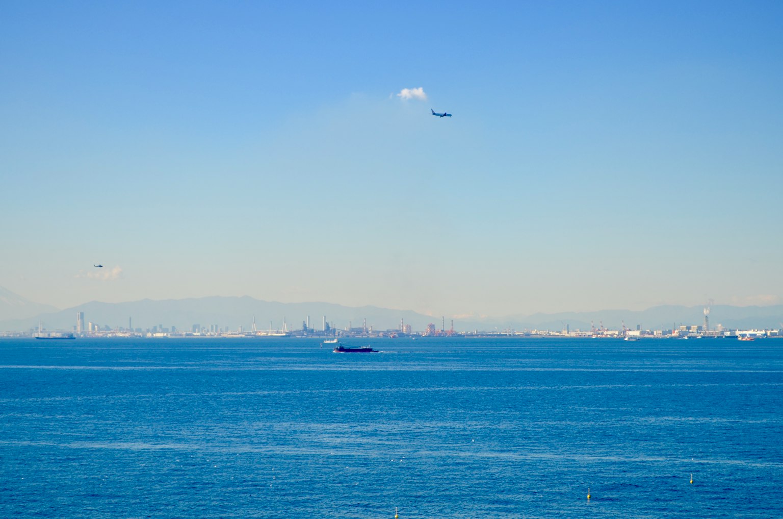 Una vista del océano azul con un horizonte urbano a lo lejos y aviones volando por encima