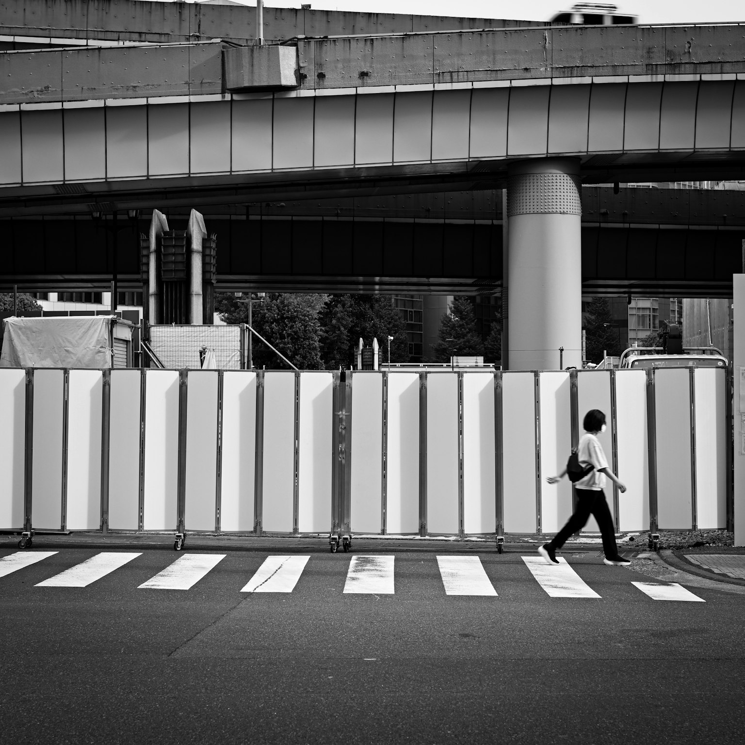 흑백 도시 환경에서 공사용 장벽이 있는 횡단보도를 걷는 사람