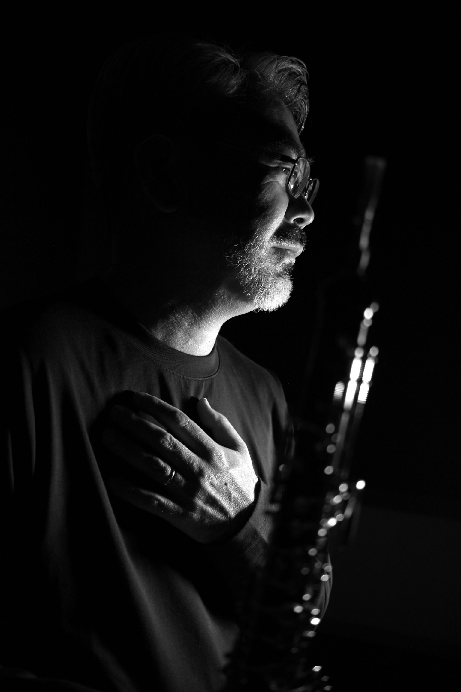 Silhouette of a man holding an instrument with hand on heart in black and white
