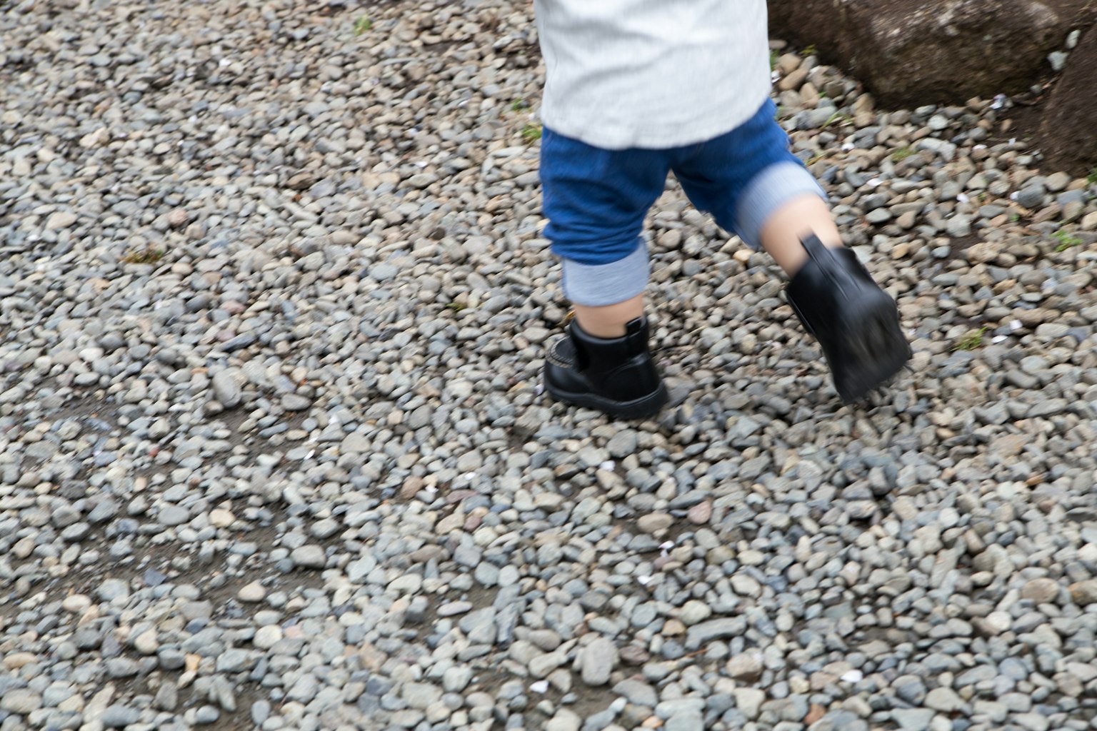 Bambino che corre su ghiaia indossando stivali neri e pantaloni corti in denim