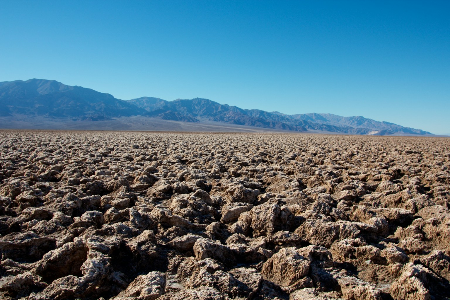 ทิวทัศน์ทะเลทรายแห้งแล้งที่มีพื้นผิวหินและภูเขาในระยะไกล