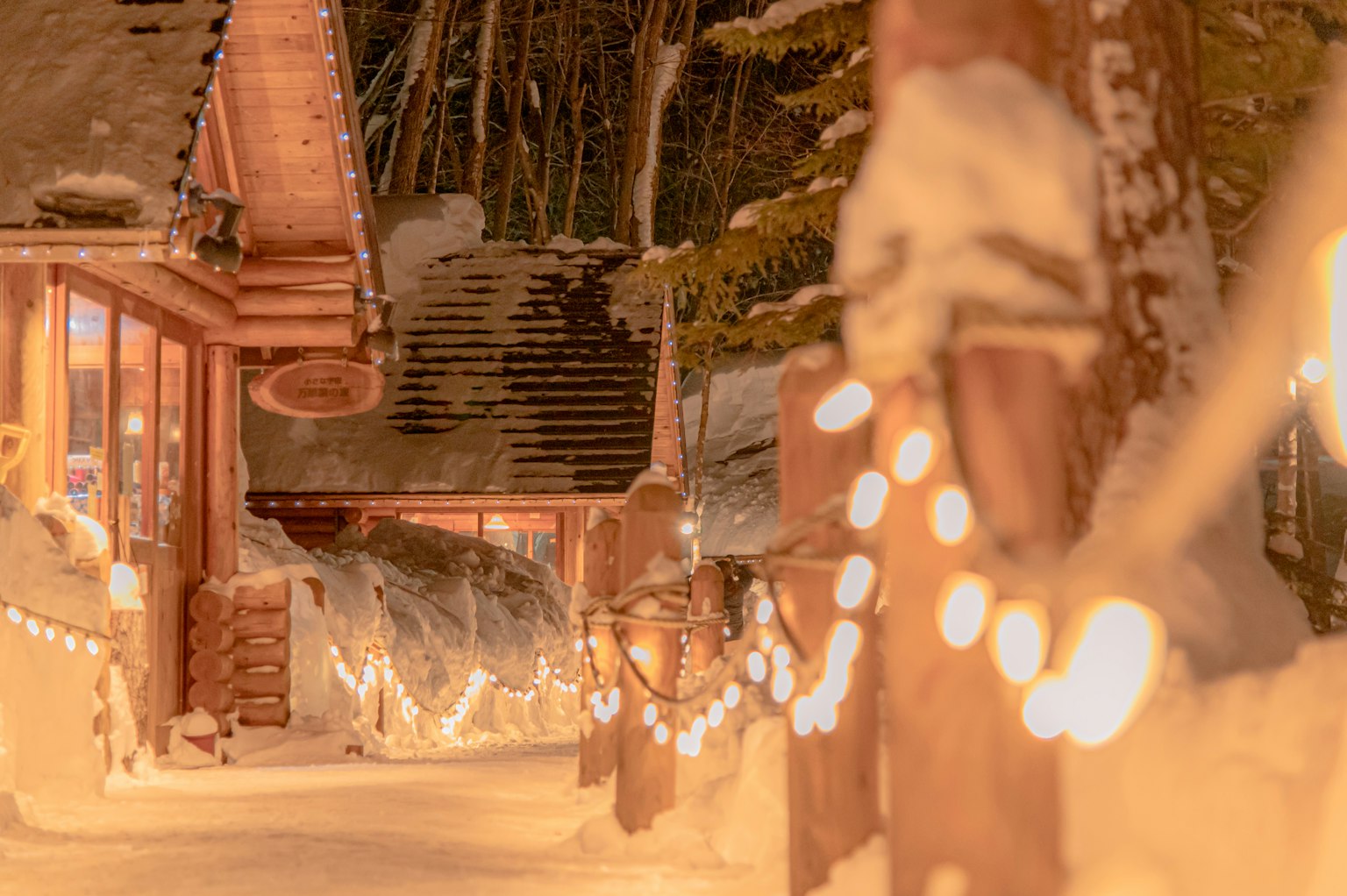 Winter scene with glowing lights along a snow-covered path and log cabins