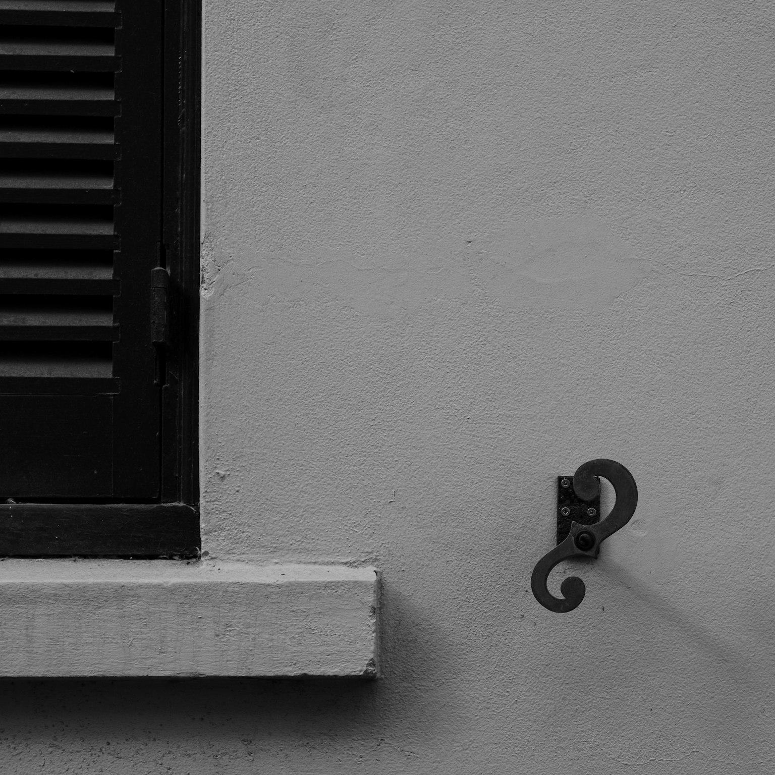 Gancio metallico decorativo attaccato a un muro grigio con persiana nera