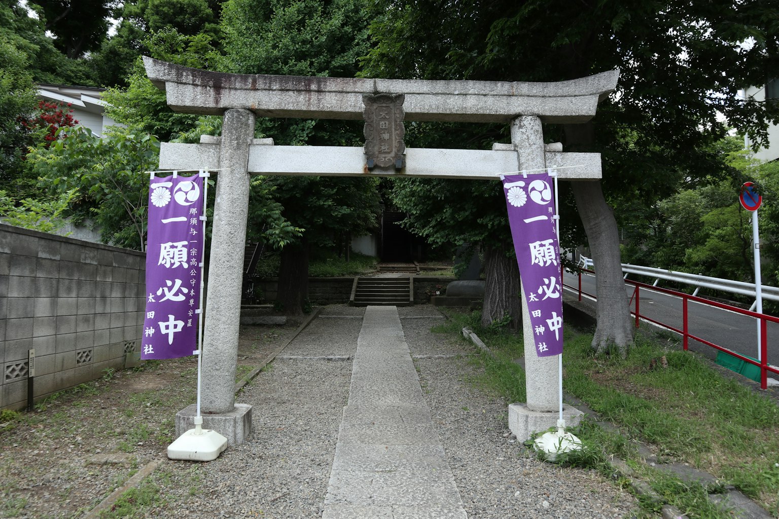 Steinernes Torii mit lila Bannern am Eingang eines Schreins