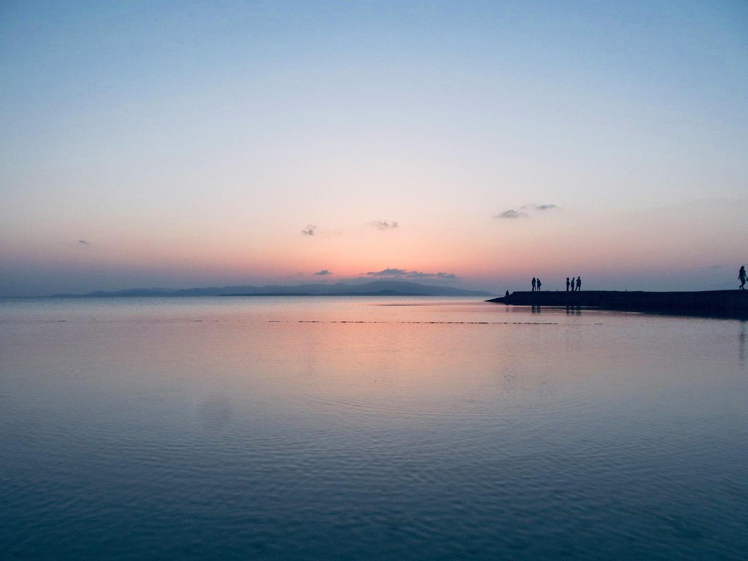 Agua tranquila que refleja un cielo de atardecer y la silueta de una montaña distante