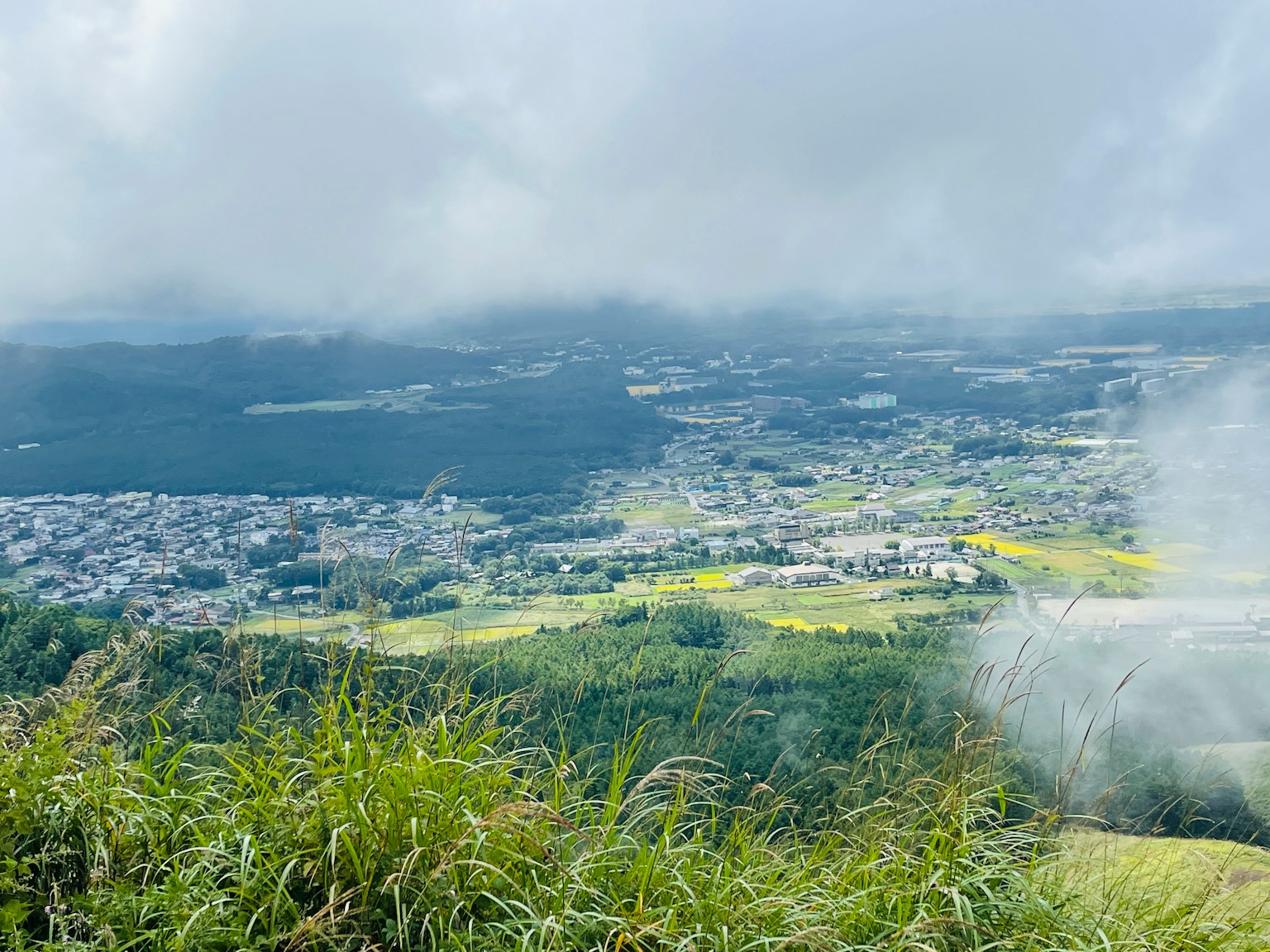 Vue panoramique depuis le sommet d'une montagne avec des collines verdoyantes, ciel nuageux et ville et champs s'étendant