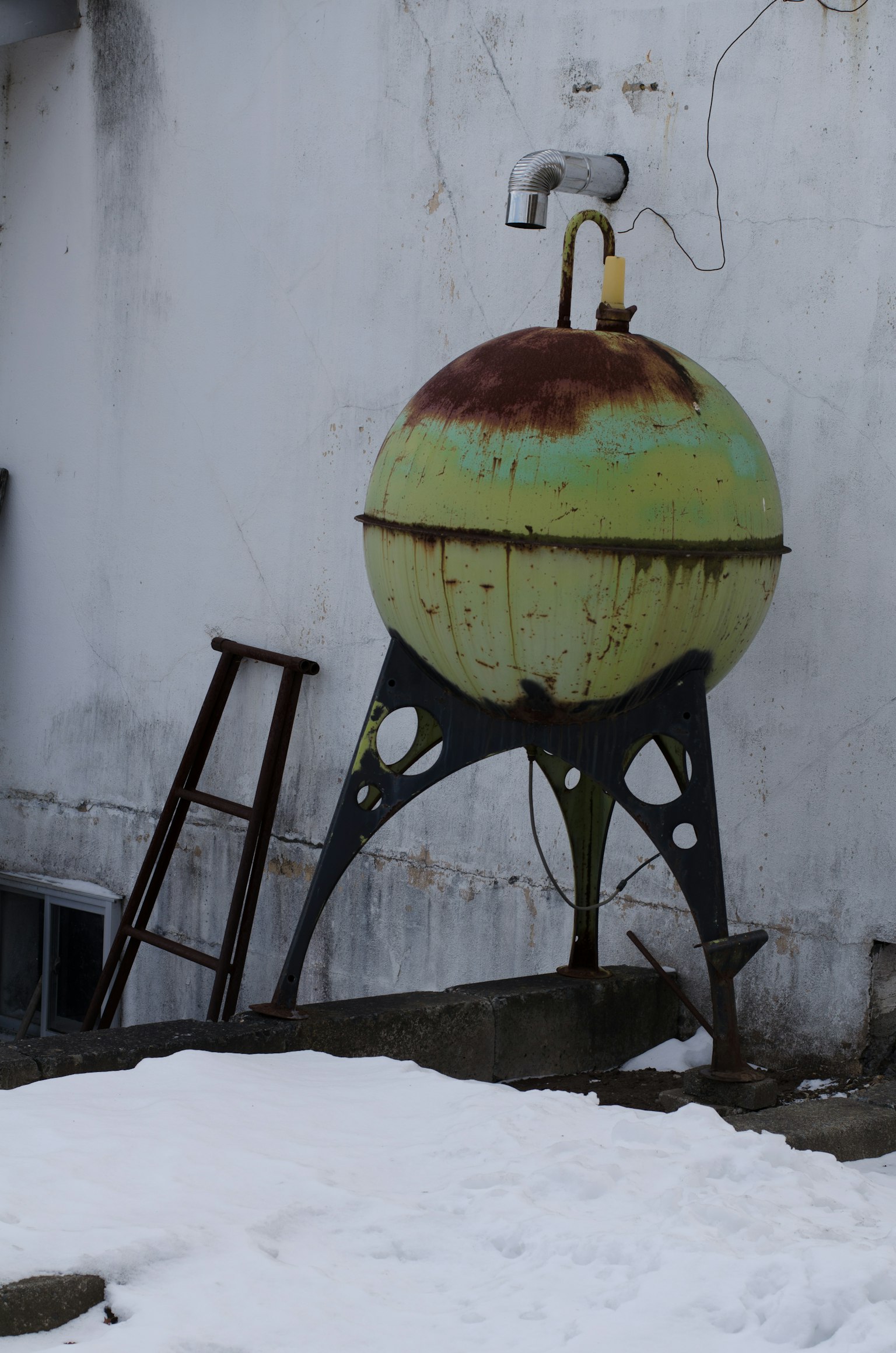 Antiguo tanque esférico verde sobre un soporte metálico negro en la nieve