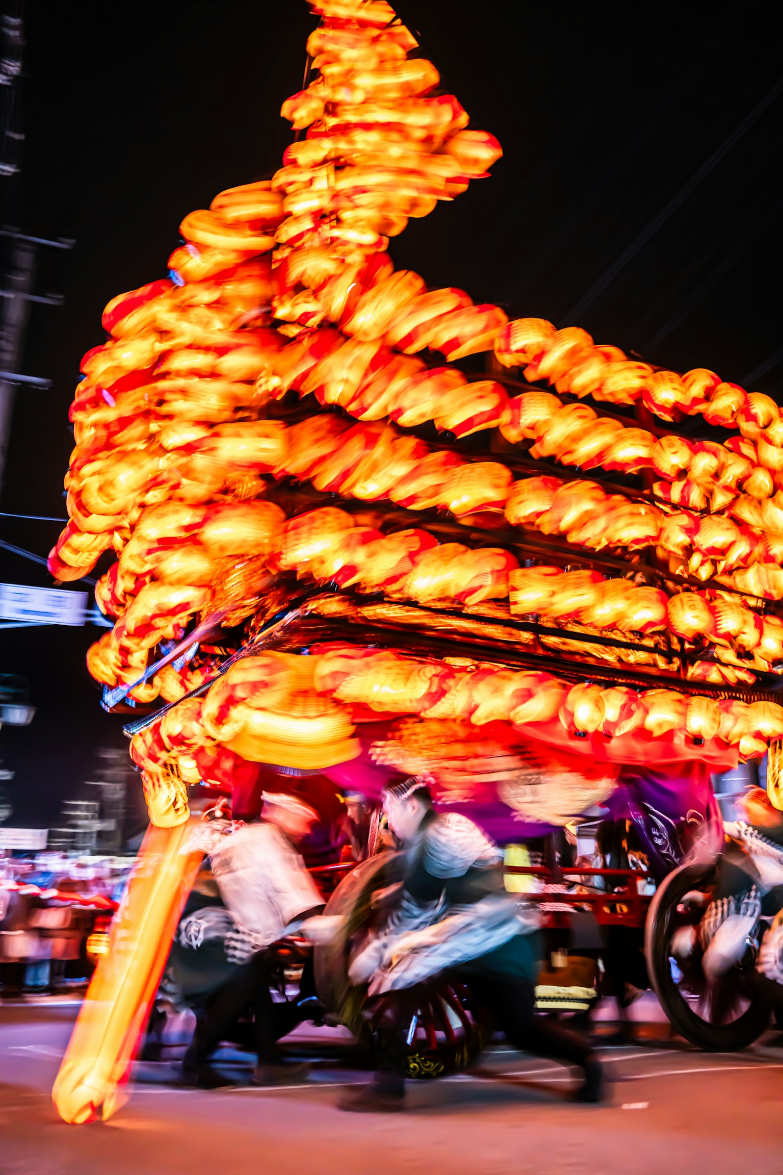 Orang-orang menarik kereta oranye yang terang saat festival malam