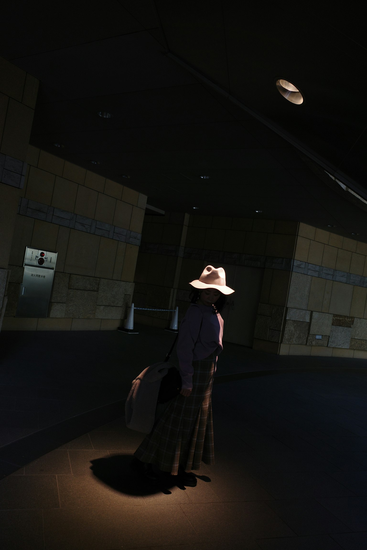 A figure standing in a dark space wearing a white hat and holding a bag