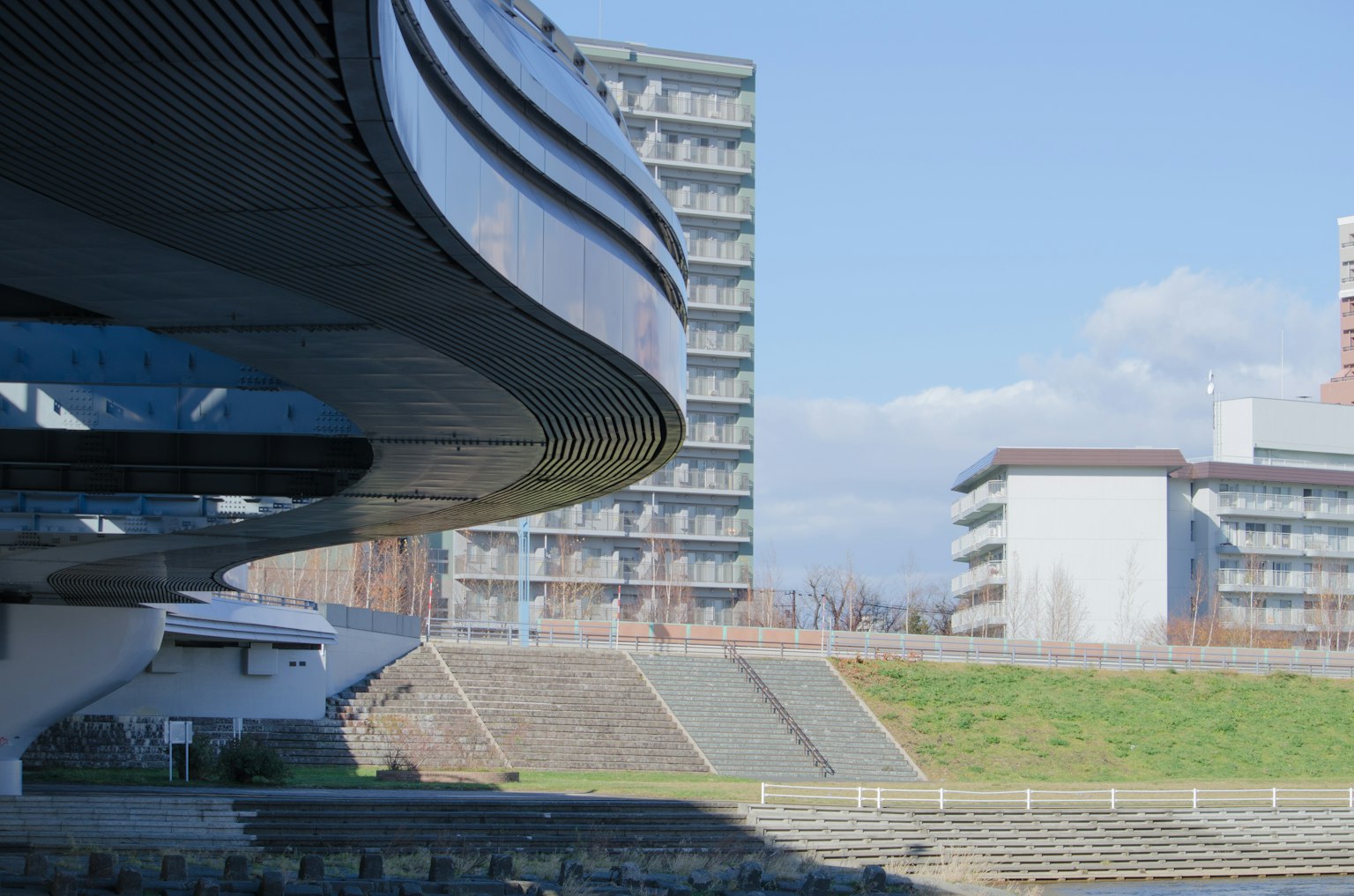 曲線建築結構，背景為現代建築和河流景觀